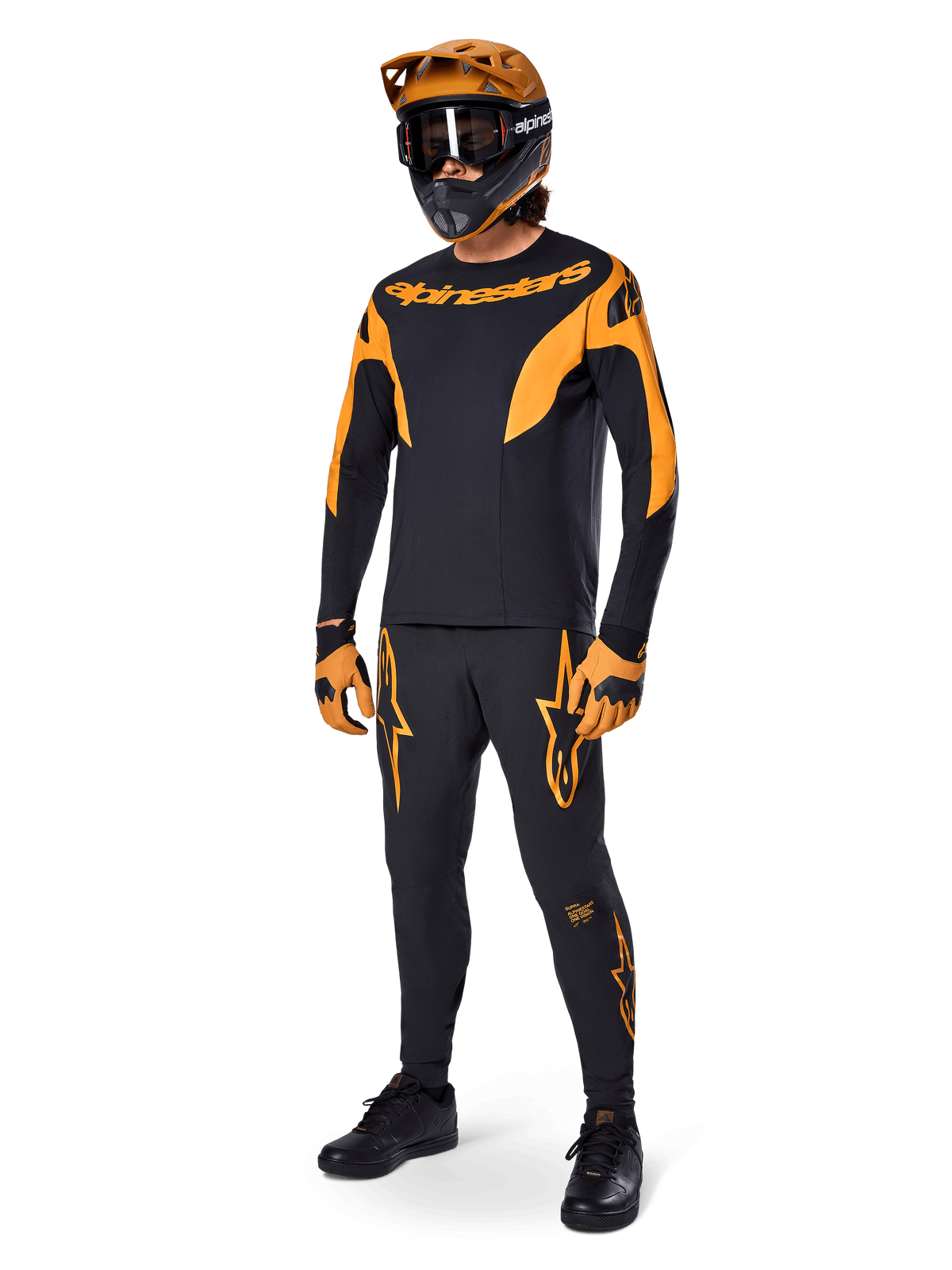 Mountain bike rider wearing complete racing gear, Alpinestars A-Supra Race Pants in black with orange accents, matching black and orange long-sleeve jersey, orange helmet with black goggles, orange and black gloves, and black shoes, professional MTB racing kit design