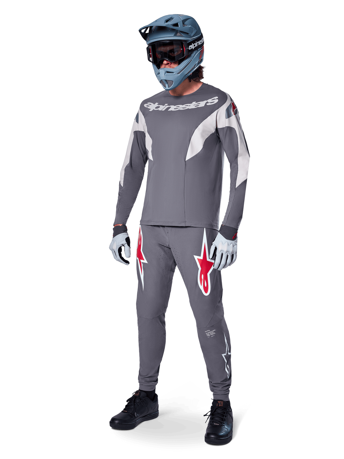 Alpinestars A-Supra Race bukser i mørkegrå, med markante røde og hvide logoer på lårene, båret af en rytter som en del af et komplet mountainbike-racersæt med matchende grå trøje, blågrå full-face hjelm og lysegrå handsker, højtydende gear til MTB-racing