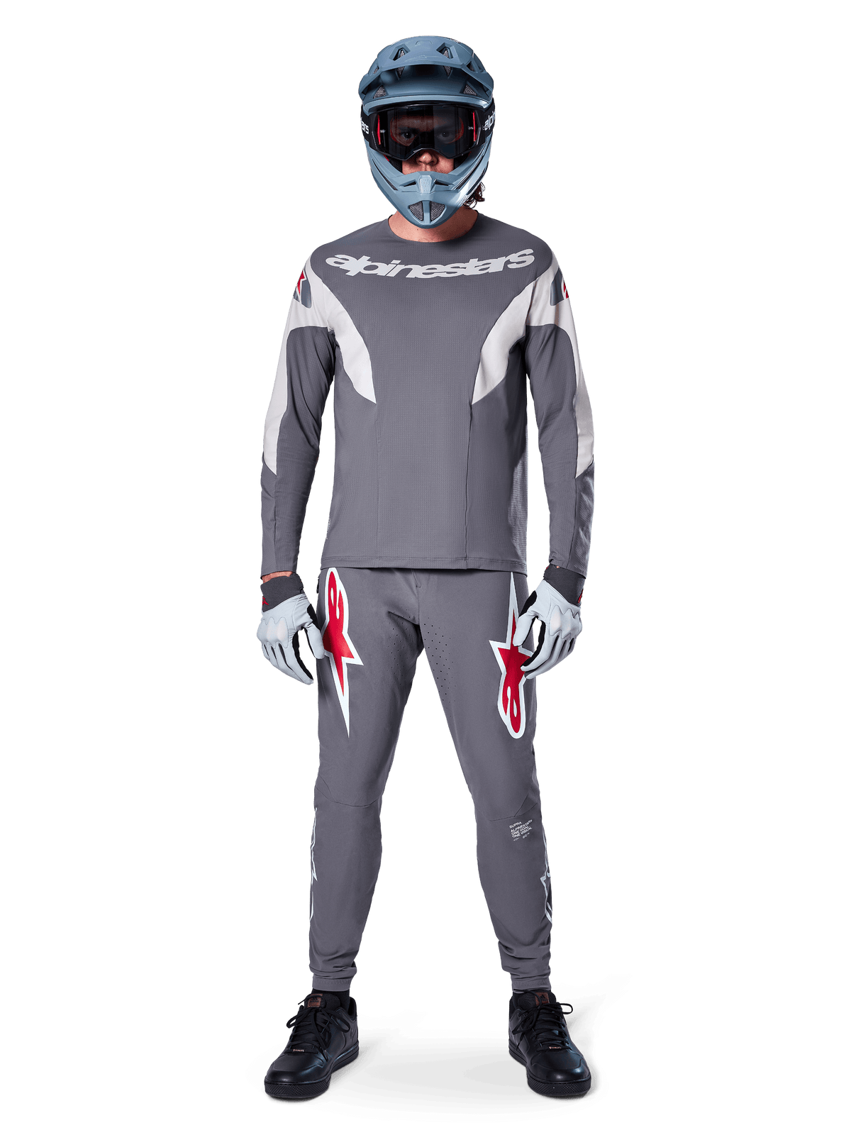 MTB-rytter iført Alpinestars A-Supra Race bukser i mørkegrå, med markante røde logo-detaljer på lårene, matchende grå jersey, blå full-face hjelm og sorte sko, komplet off-road racersæt