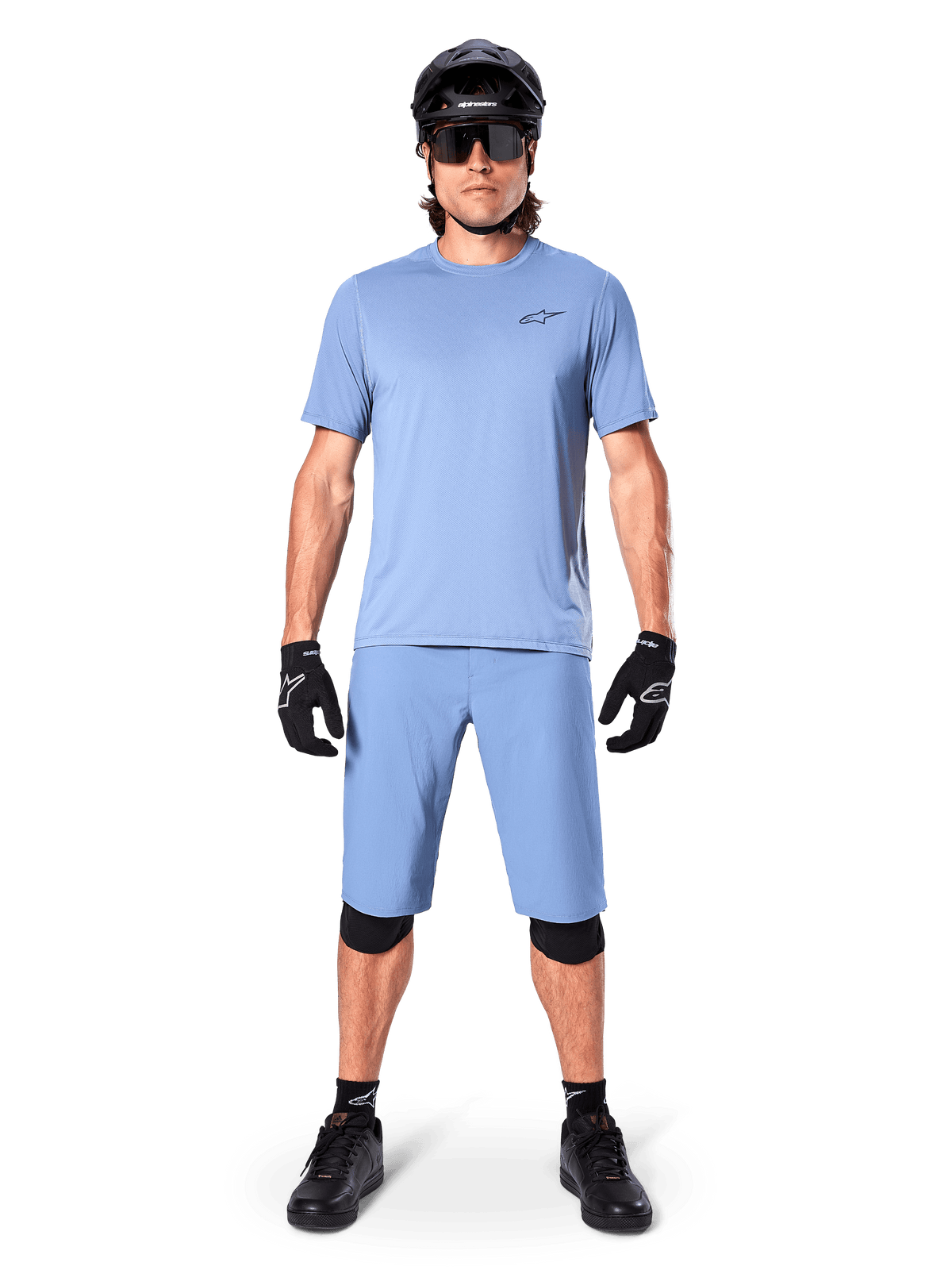 Model iført Alpinestars A-Dura shorts i Infinity Blue, matchende lyseblå jersey, sort mountainbikehjelm, sorte solbriller, sorte handsker og knæbeskyttere, komplet MTB-outfit til trailkørsel