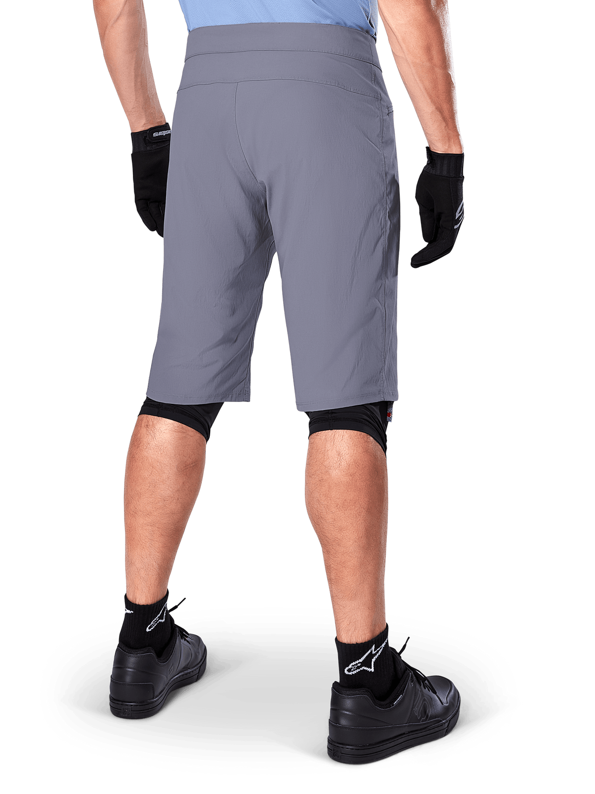 Alpinestars A-Dura Shorts, mørkegrå mountainbike-shorts, set bagfra på en rytter, bæres med sorte handsker, sorte knæ-liners og sorte sokker med Alpinestars-logo, holdbar konstruktion til terrænkørsel