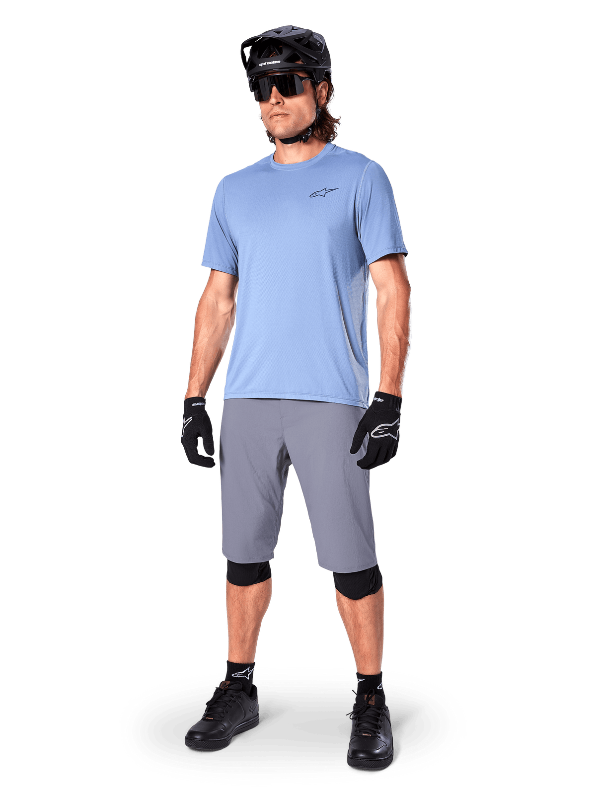Alpinestars A-Dura shorts, MTB-shorts, mørkegrå, båret af en rytter med lyseblå trøje, sort MTB-hjelm, sorte handsker og knæbeskyttere, komplet mountainbike-outfit til trail- og terrænkørsel