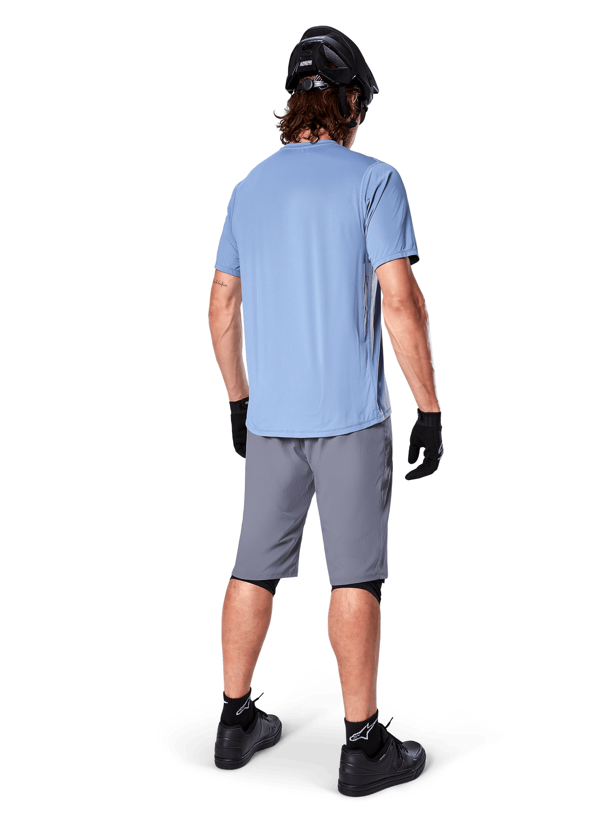 Alpinestars A-Dura shorts, mørkegrå MTB-shorts, set bagfra, båret med en lyseblå kortærmet trøje og sort mountainbike-hjelm, sorte handsker og strømper med sorte sko, funktionelt og holdbart gear til terrænkørsel