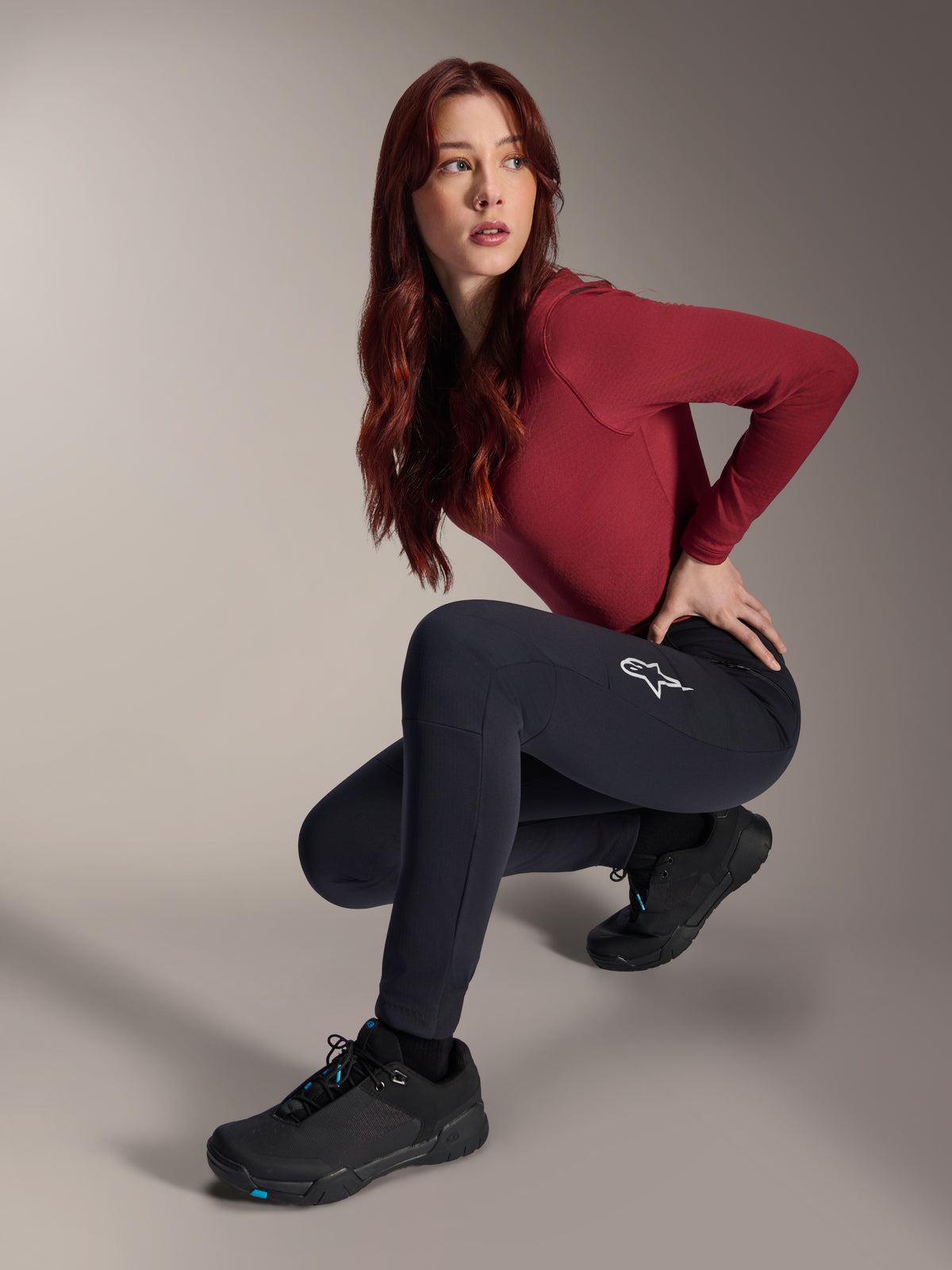 Alpinestars Stella A-Dura termobukser, MTB-bukser til damer, sort, båret af en model siddende på hug med en bordeauxrød langærmet top og sorte cykelsko, med et hvidt stjernelogo på låret, holdbar og varm konstruktion til terrænkørsel i koldt vejr