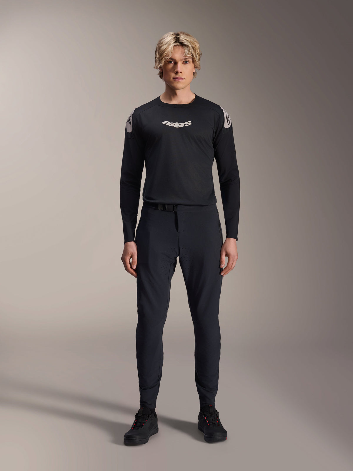 Mandlig model iført Alpinestars A-Aria Polartec Elite langærmet jersey i sort, med hvidt Astars-logo på brystet og branding på skuldrene, parret med sorte tekniske MTB-bukser og sko, performance mountainbike-udstyr