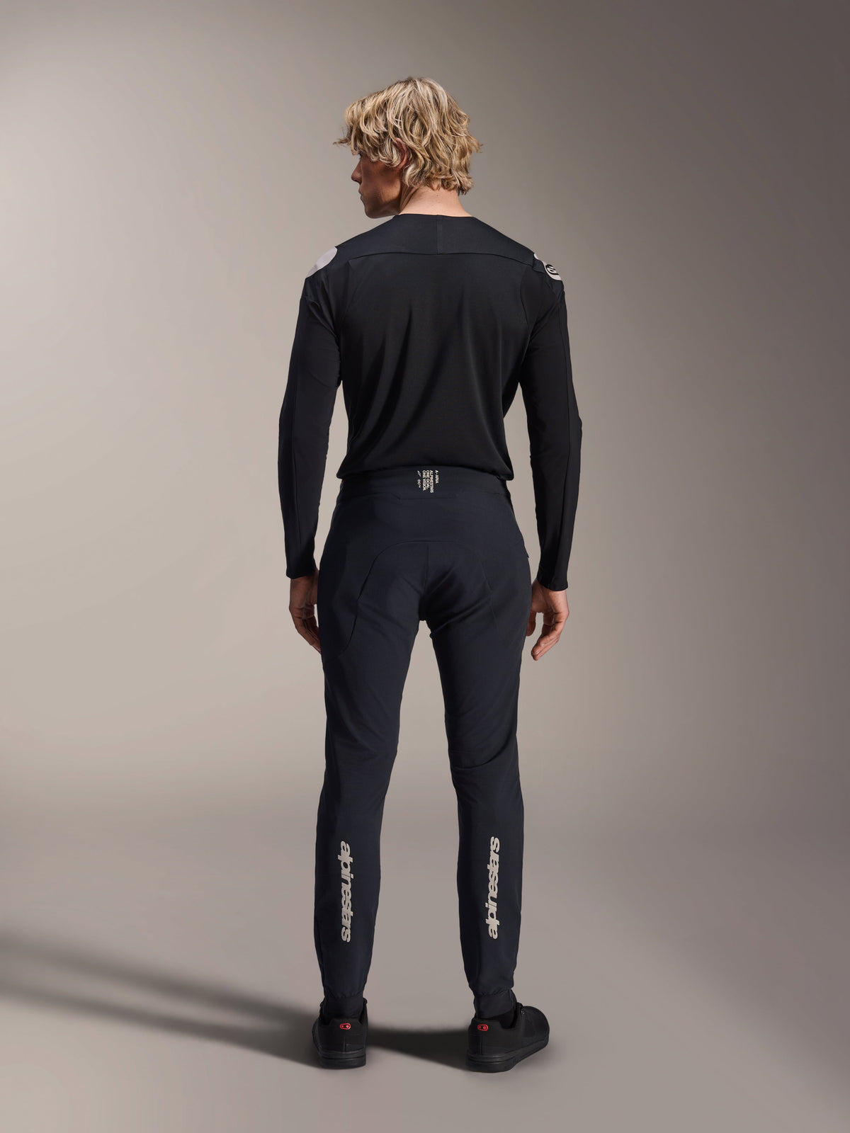 Alpinestars A-Aria Polartec Elite langærmet jersey, sort MTB-jersey, set bagfra båret med matchende sorte bukser, performance-pasform til mountainbike, med teknisk svedtransporterende stof og diskret branding på den nederste del af ryggen