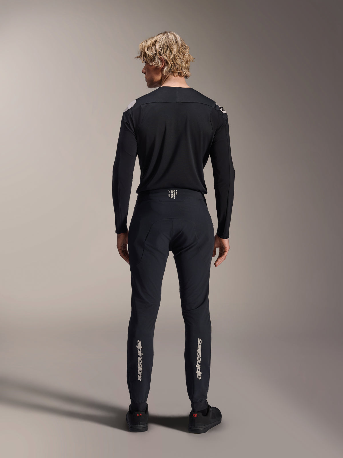 Alpinestars A-Aria Elite bukser, Black Titanium, set bagfra på mandlig model, med sølv Alpinestars-branding på underbenene, tekniske MTB-bukser med performance-pasform og fugttransporterende detalje i linningen