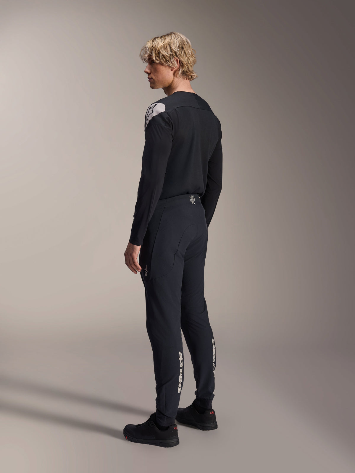 Alpinestars A-Aria Polartec Elite langærmet jersey, sort, vist på en model fra en skrå bagfra-profil, med et hvidt logo på skulderen, kombineret med matchende sorte cykelbukser for et professionelt MTB-outfit.