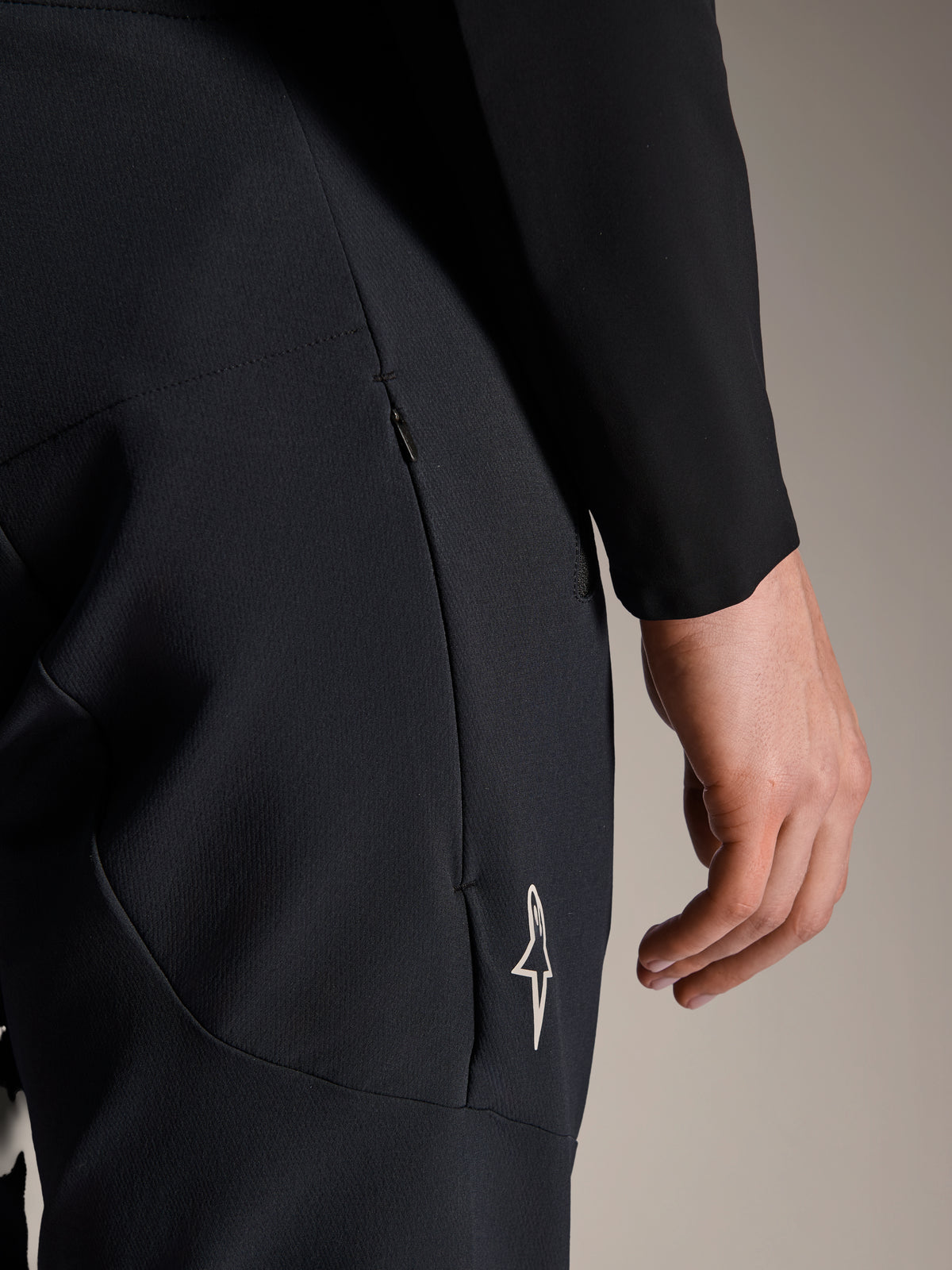 Nærbillede af Alpinestars A-Aria Elite bukser i Black Titanium, med en sidelomme med lynlås og lille hvidt stjerne-logo, tekniske mountainbike-bukser designet til performance-cykling