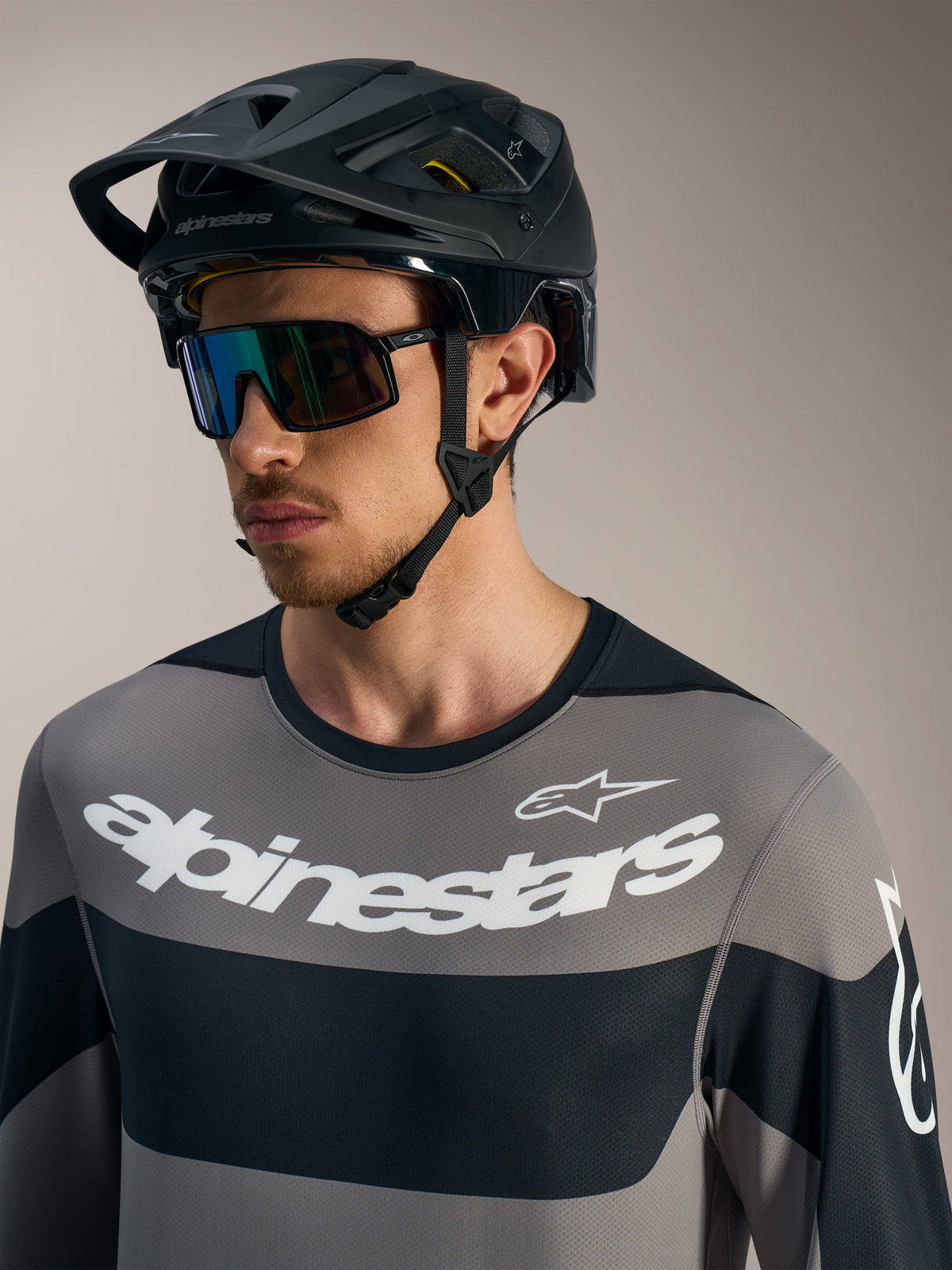 Alpinestars A-Dura Race trøje, langærmet grå med hvide logoer, sort MTB-hjelm og performance-solbriller.
