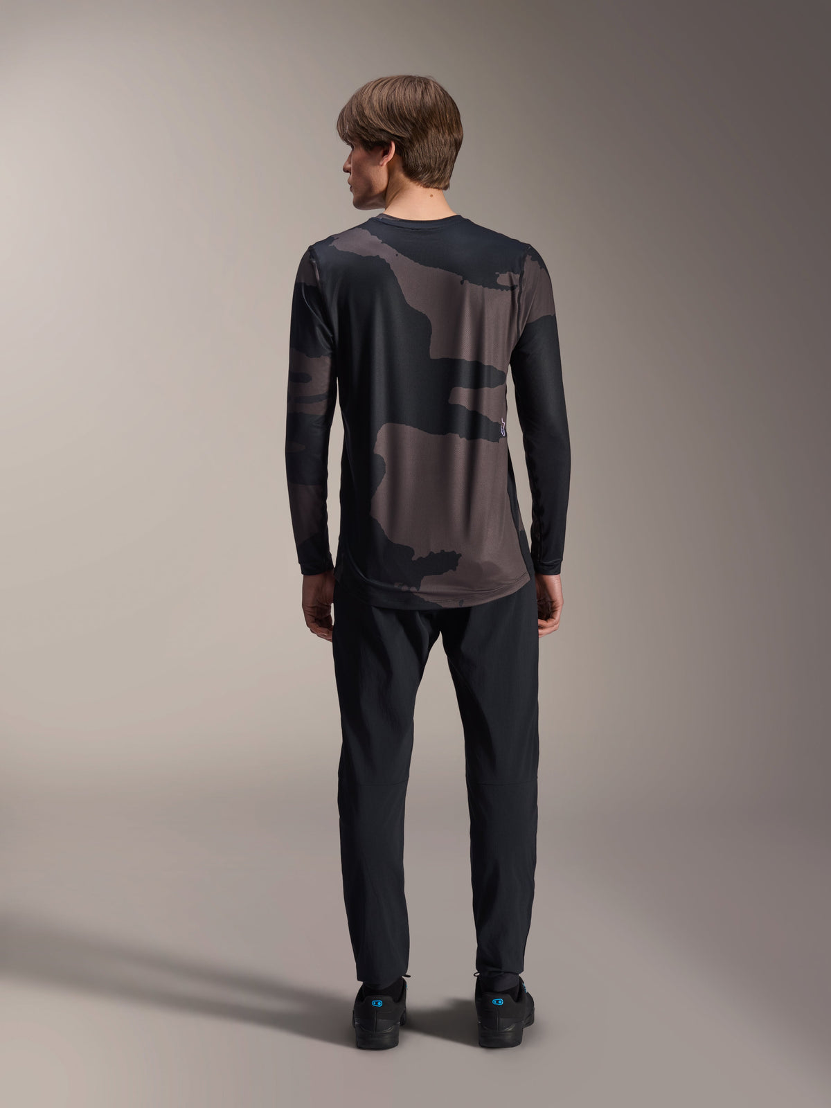 Alpinestars A-Dura Hollow Camo Long Sleeve Jersey, Black Camo, back view worn with black pants, featuring a dark camouflage pattern and dropped rear hem for MTB coverage.