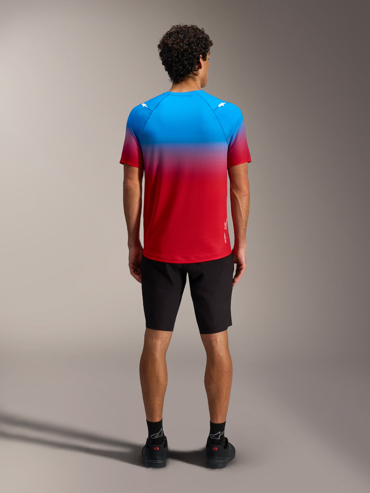 A-Dura ASTARS Jersey 2.0, kortærmet MTB-trøje med rød og blå farveovergang, set bagfra med sorte shorts.