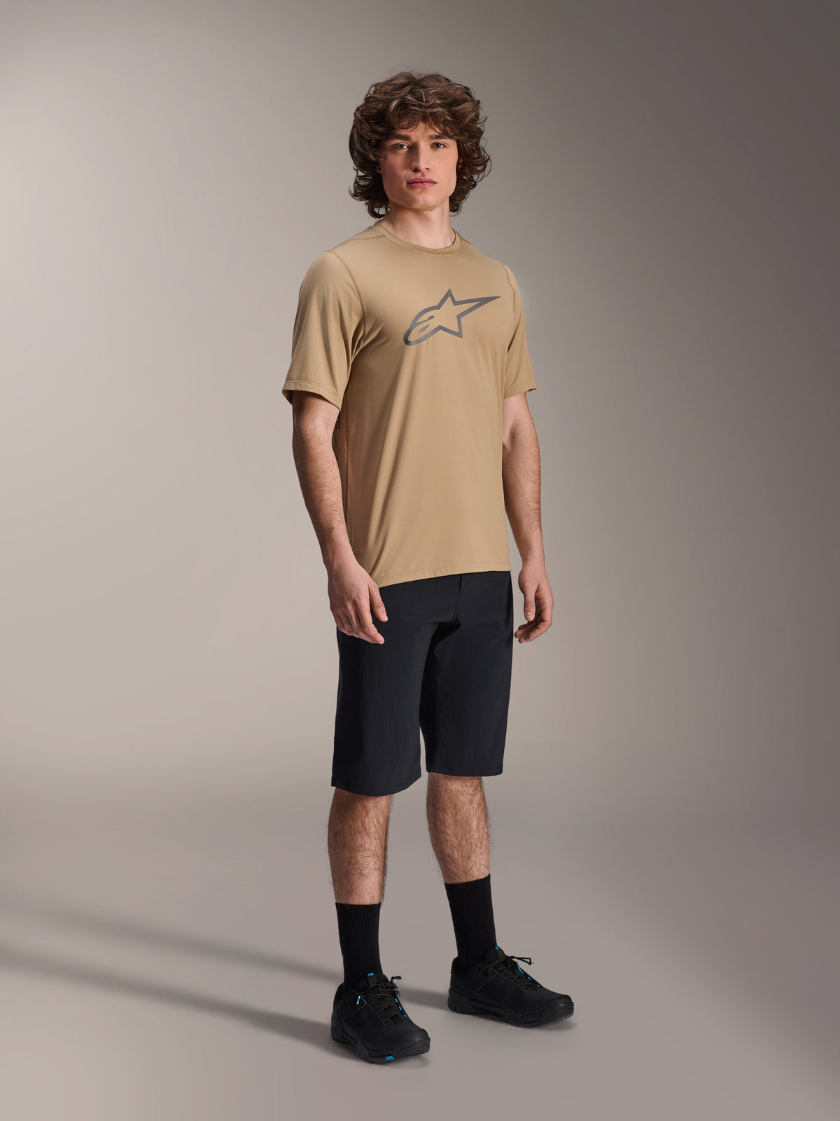 Male model wearing Alpinestars A-Dura Liner Shorts in Black, paired with a tan A-Dura SS Jersey featuring a grey Astars logo, black cycling socks and mountain bike shoes, complete off-road cycling outfit