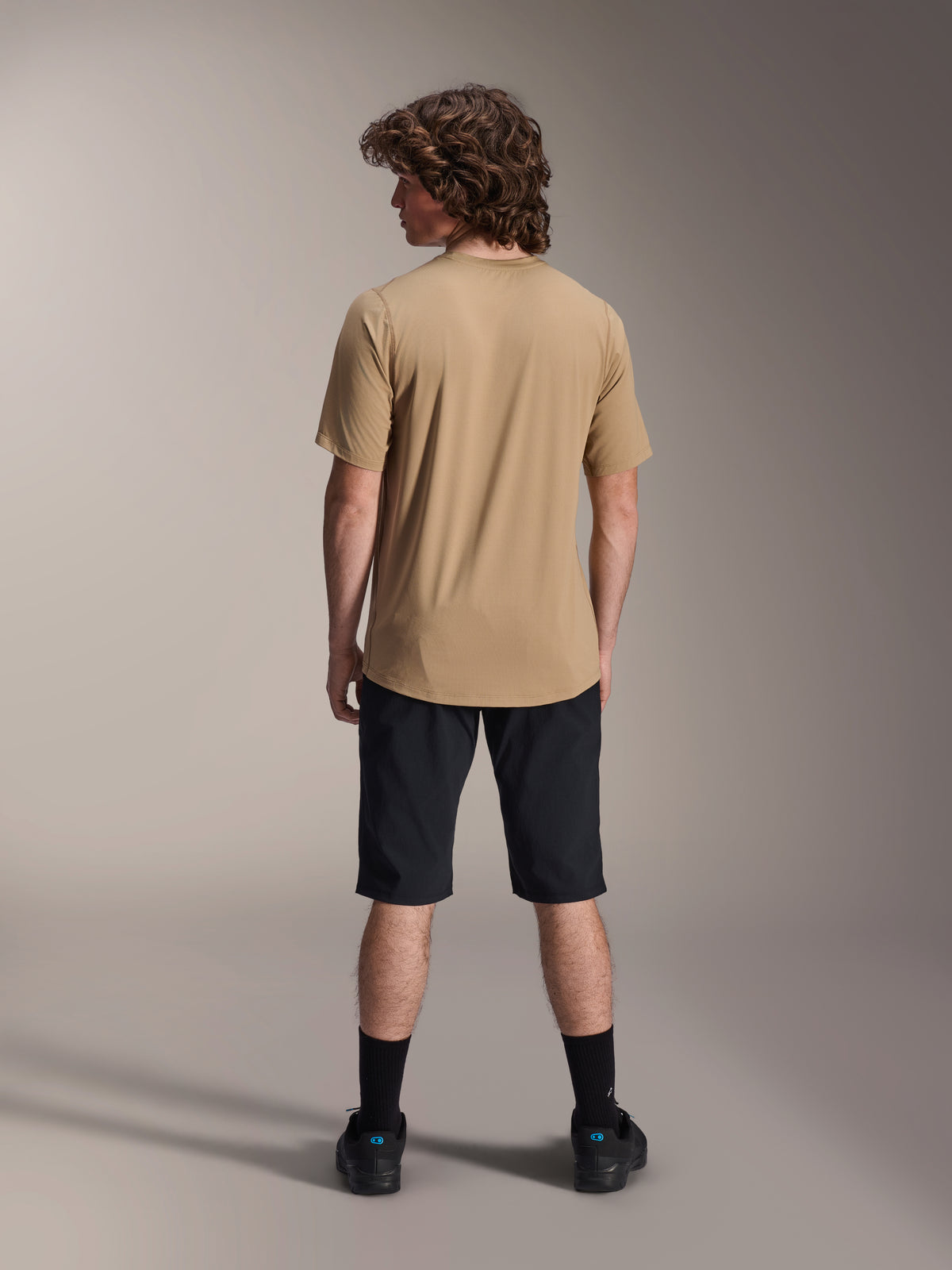 Mandlig model set bagfra iført Alpinestars A-Dura shorts i sort og en beige A-Dura kortærmet jersey, sorte strømper og mountainbike-sko, funktionelt MTB-trailoutfit