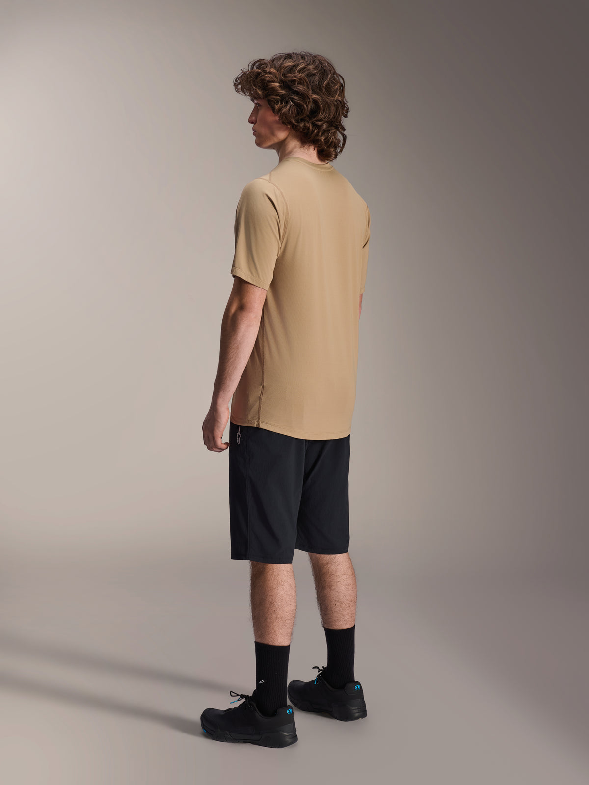 Alpinestars A-Dura shorts, mountainbike-shorts, sorte, kombineret med en sandfarvet A-Dura kortærmet jersey og sorte cykelsko, med almindelig pasform og holdbar konstruktion til terrænkørsel, set bagfra fra siden