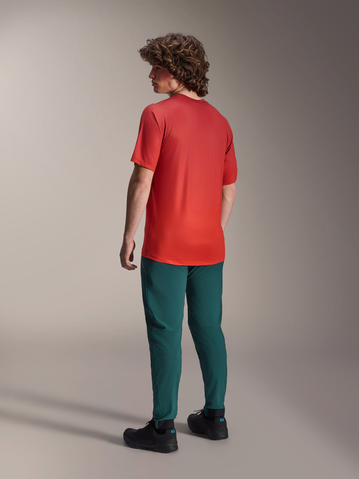 Model set bagfra iført Alpinestars A-Dura bukser i Dark Pine grøn og en rød A-Dura Rise kortærmet jersey, med almindelig pasform og elastiske manchetter, performance mountainbike-tøj til terrænkørsel