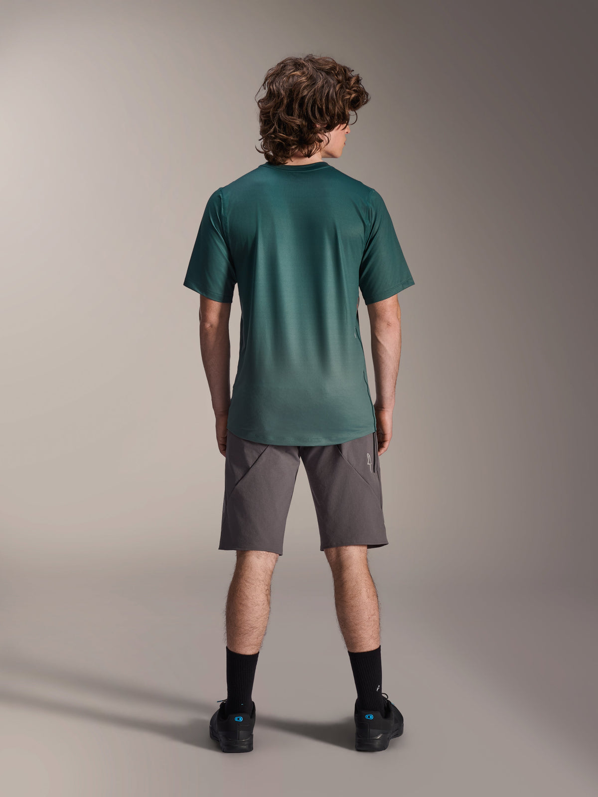 Alpinestars A-Dura Rise kortærmet jersey, Silver Pine grøn, set bagfra på en mandlig model iført grå shorts og sorte strømper, med en længere drop tail og almindelig pasform til mountainbike