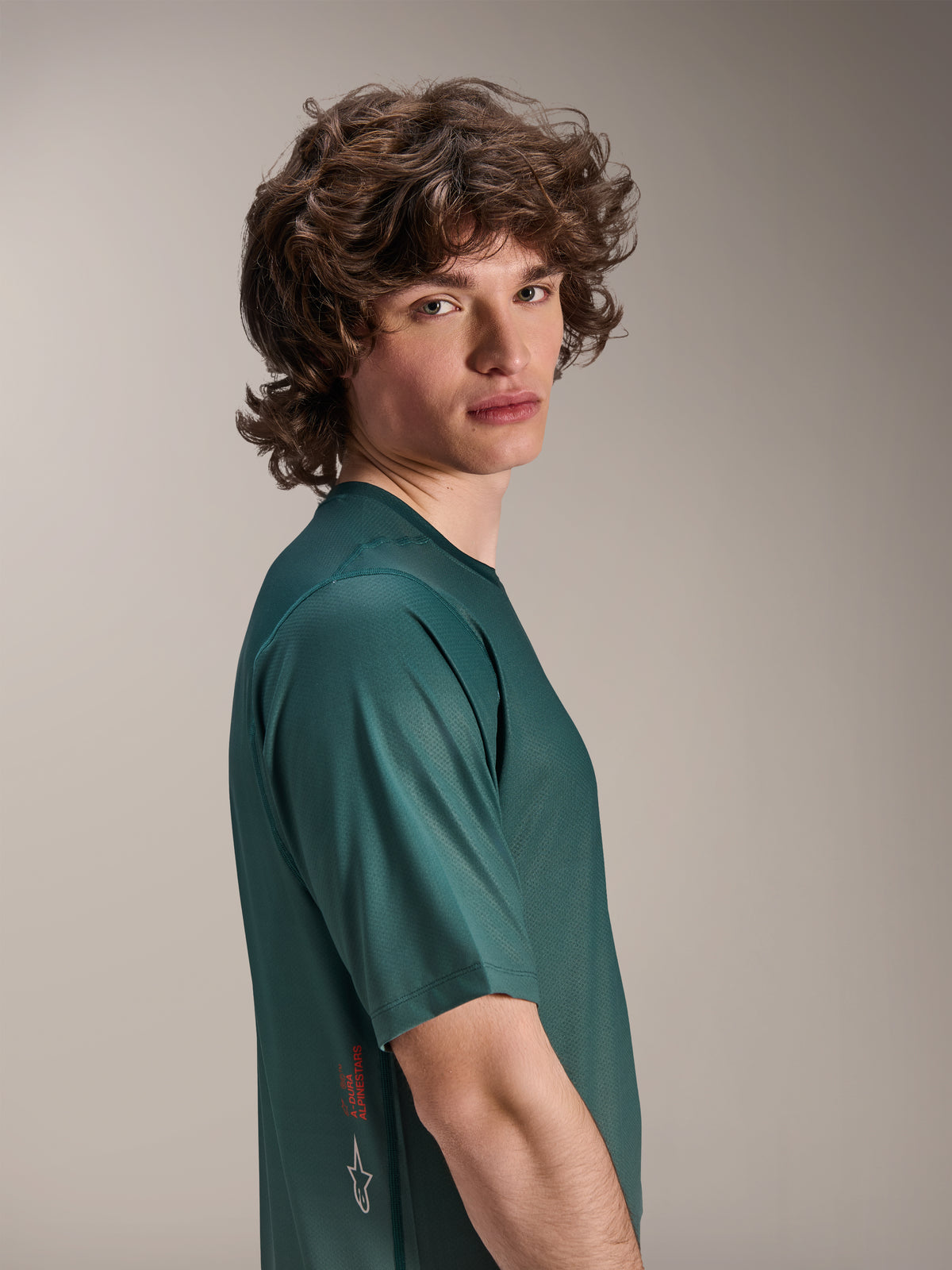 Alpinestars A-Dura Rise Jersey, kortærmet MTB-jersey, Silver Pine grøn, mandlig model iført fugttransporterende jacquard-materiale, rødt A-Dura Alpinestars-ordmærke og hvidt logo på siden, high-performance trail-udstyr