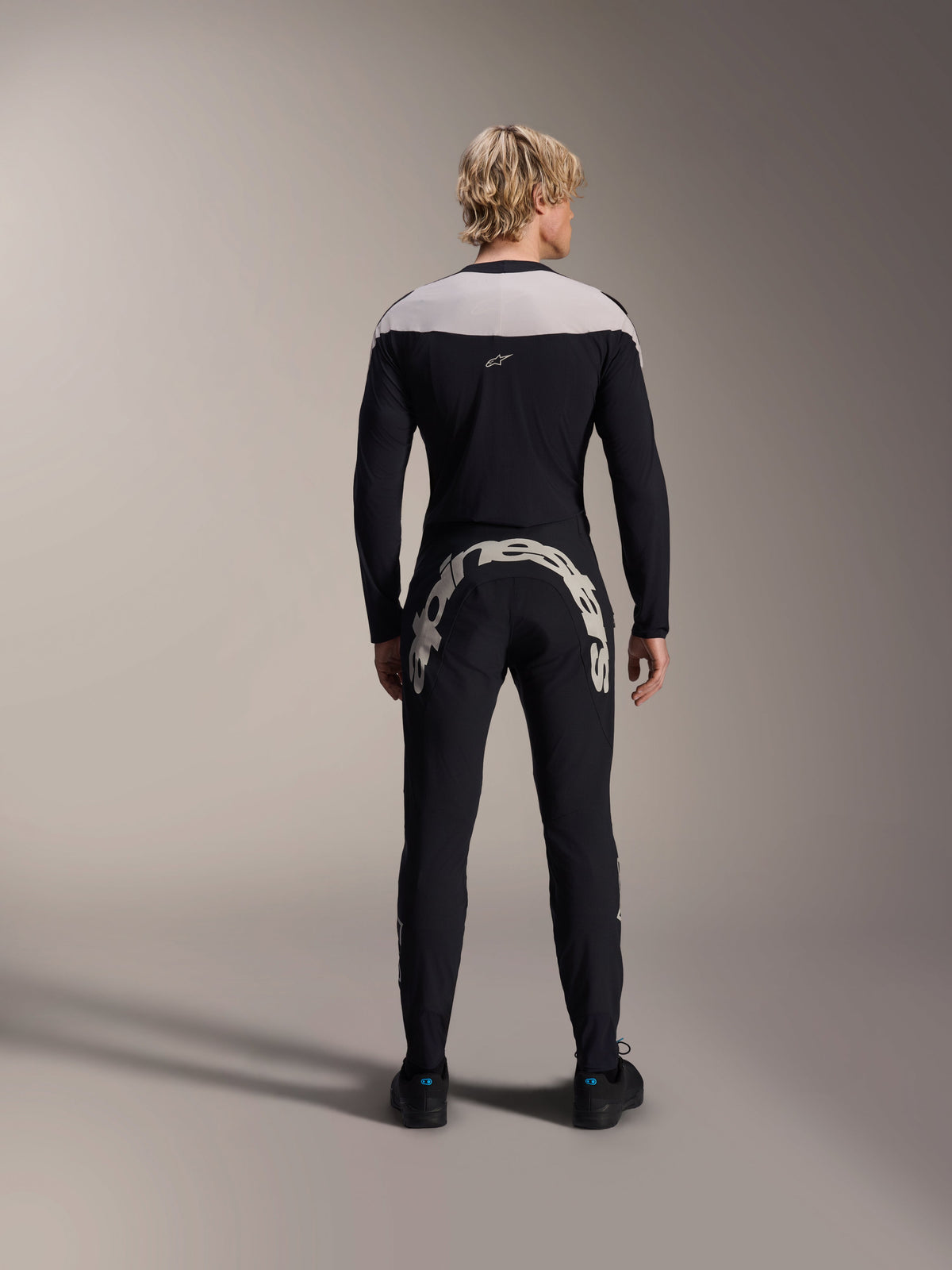 Mand set bagfra iført Alpinestars A-Supra Melt langærmet trøje i sort, lysegråt skulderpanel, kombineret med sorte MTB-bukser med et stort Alpinestars-logo hen over bagdelen, performance mountainbike-udstyr