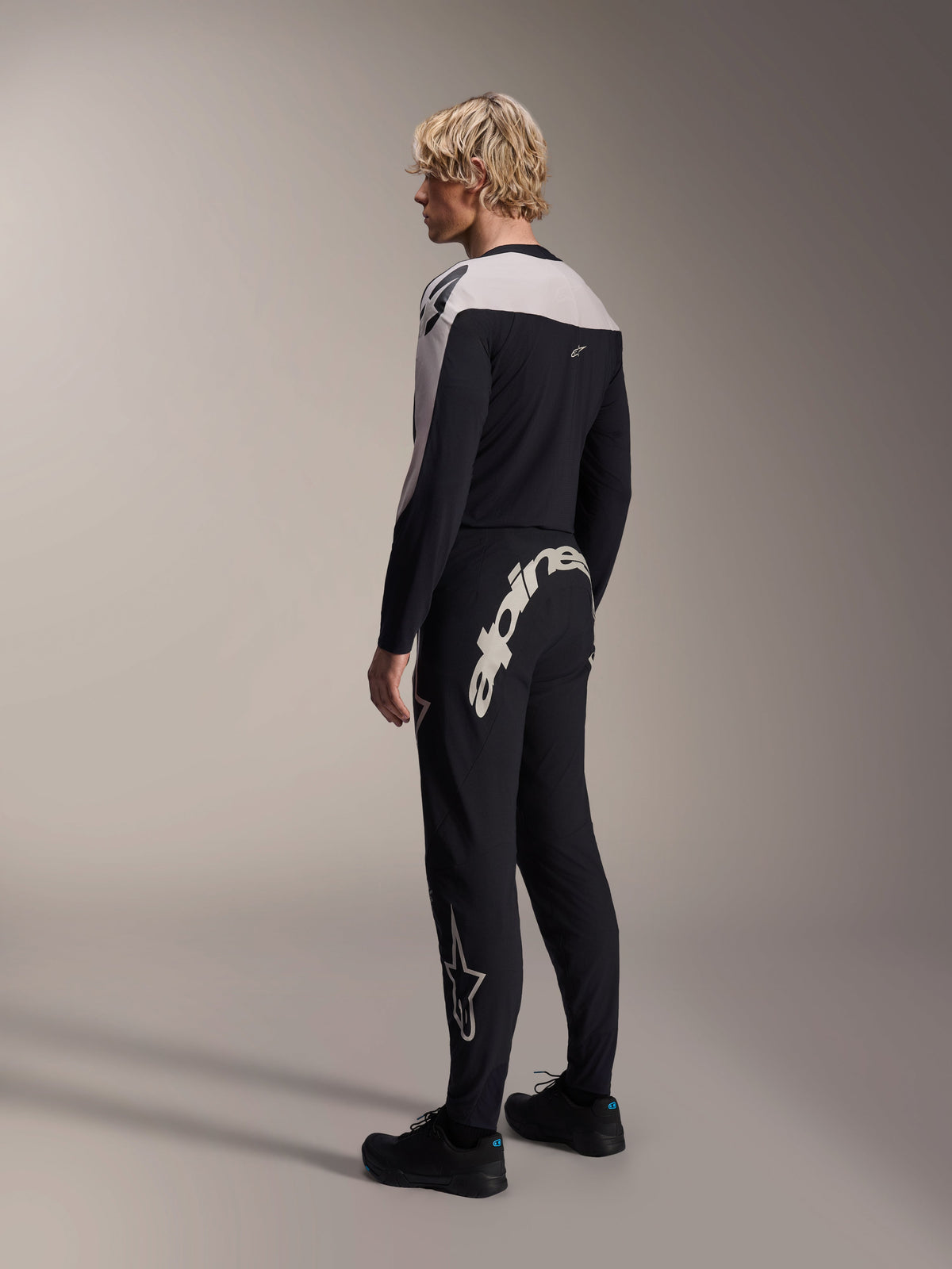 Alpinestars A-Supra Melt langærmet trøje, sort med hvide skulderpaneler, båret af en model set bagfra og fra siden, parret med sorte mountainbike-bukser med et stort hvidt ordmærke, performance MTB-racerudstyr