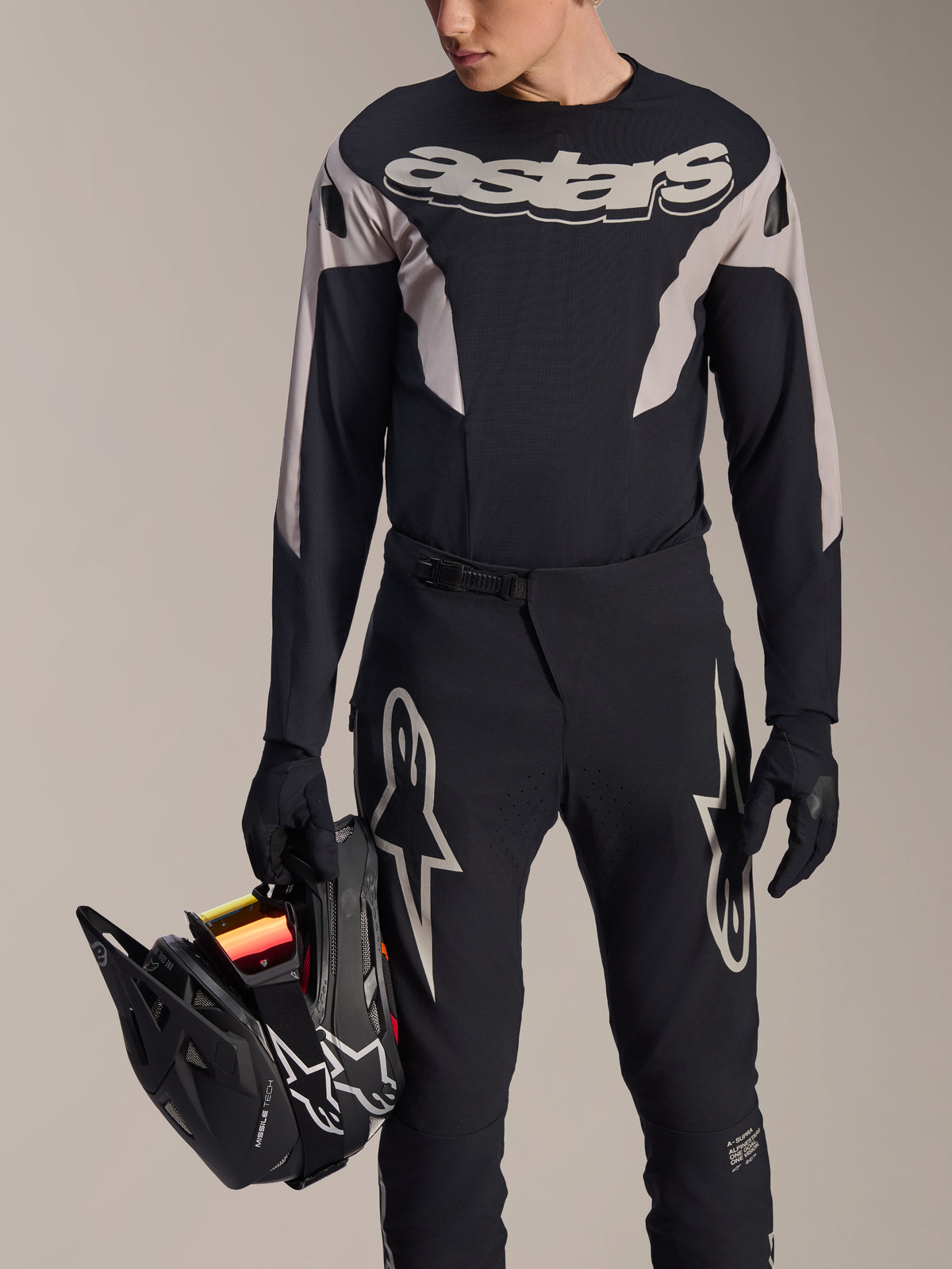 Alpinestars A-Supra Melt langærmet trøje, sort med grå grafiske paneler og markant 'astars'-ordmærke på brystet, bæres med sorte mountainbike-bukser og handsker, mens der holdes en sort full-face hjelm, performance MTB-racerudstyr