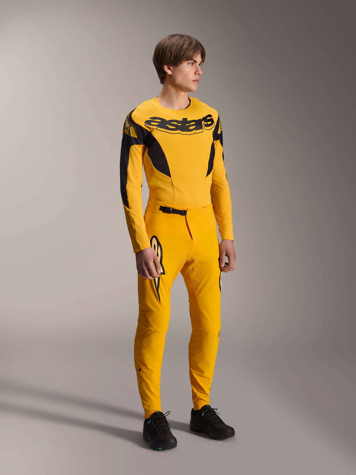 Alpinestars Limited Edition A-Supra Melt Gold Gear-Set, mandlig model iført gul langærmet MTB-trøje med markant sort branding på brystet, matchende gule bukser med laserskåret ventilation og sorte detaljer, komplet mountainbike-racerkit.