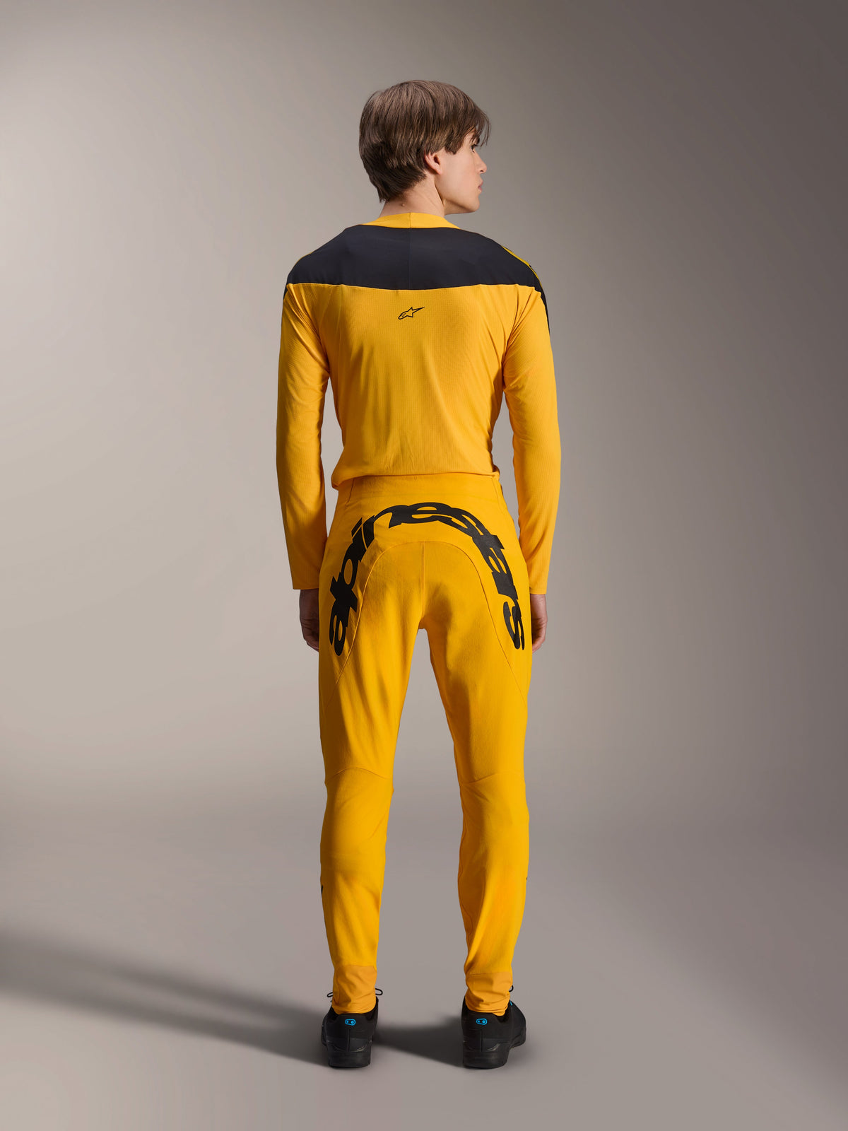 Alpinestars Limited Edition A-Supra Melt Gold Jersey, Long Sleeve MTB Jersey, Dark Yellow, back view, featuring black shoulder panels, worn with matching yellow pants with large black branding on the rear, performance cycling gear