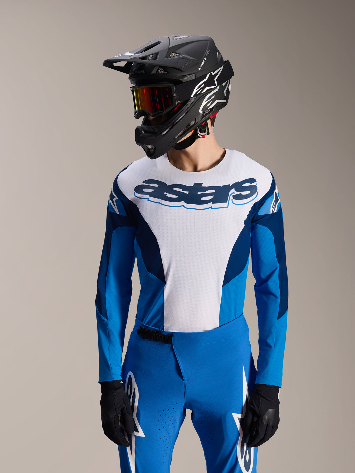 Model iført Alpinestars A-Supra Melt langærmet jersey i blå og hvid med 'astars' tekstlogo på brystet, stylet med matchende blå MTB-bukser, sort full-face hjelm og goggles, komplet mountainbike-raceroutfit.