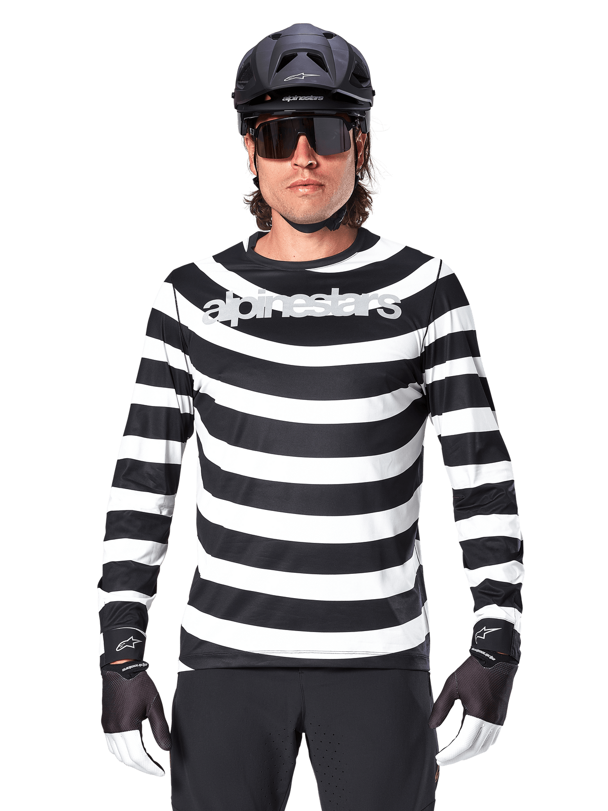 Mandlig cyklist iført Alpinestars A-Aria Oscar langærmet jersey, sorte og hvide vandrette striber, reflekterende Alpinestars-logo på brystet, stylet med sort MTB-hjelm, cykelbriller og performance-handsker