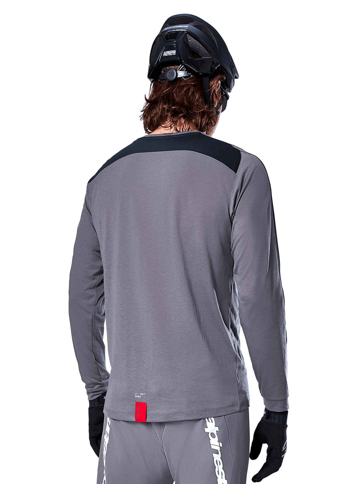 Alpinestars A-Dura Dri Astar langærmet jersey, mørkegrå MTB-trøje set bagfra, med et sort skulderpanel og lille rødt mærke, båret med en sort mountainbikehjelm og handsker.