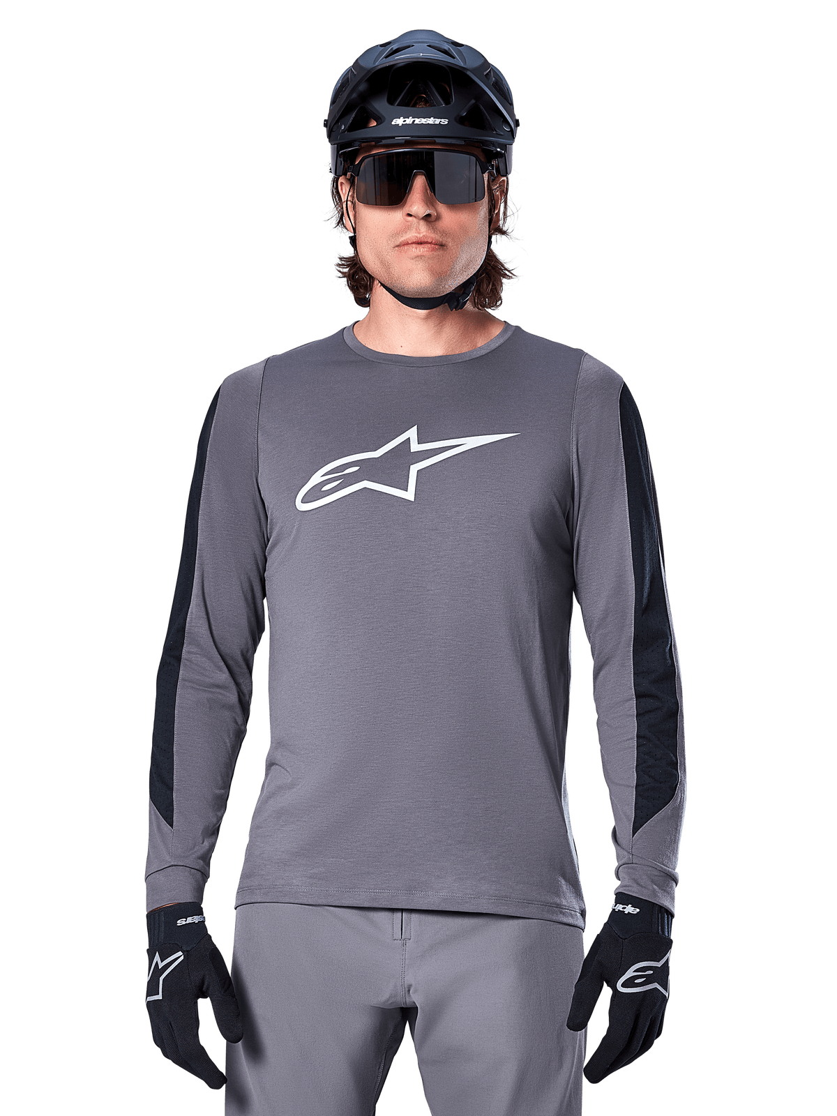 Alpinestars A-Dura Dri Astar langærmet jersey, mørkegrå, med et stort hvidt Astar-logo på brystet og sorte mesh-paneler på armene, båret af en rytter med en sort mountainbikehjelm og performance-solbriller, MTB-cykeltøj