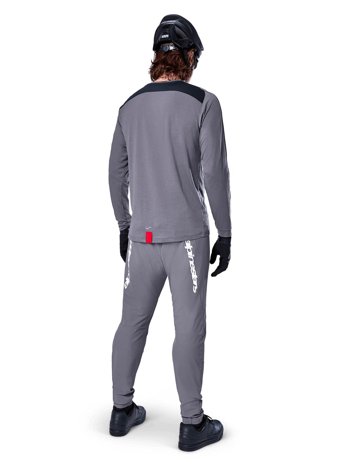 Alpinestars A-Dura Dri Astar langærmet jersey, mørkegrå, set bagfra af rytter iført matchende bukser og sort hjelm, har sorte skulderpaneler og et lille rødt mærke ved kanten, teknisk off-road cykeludstyr
