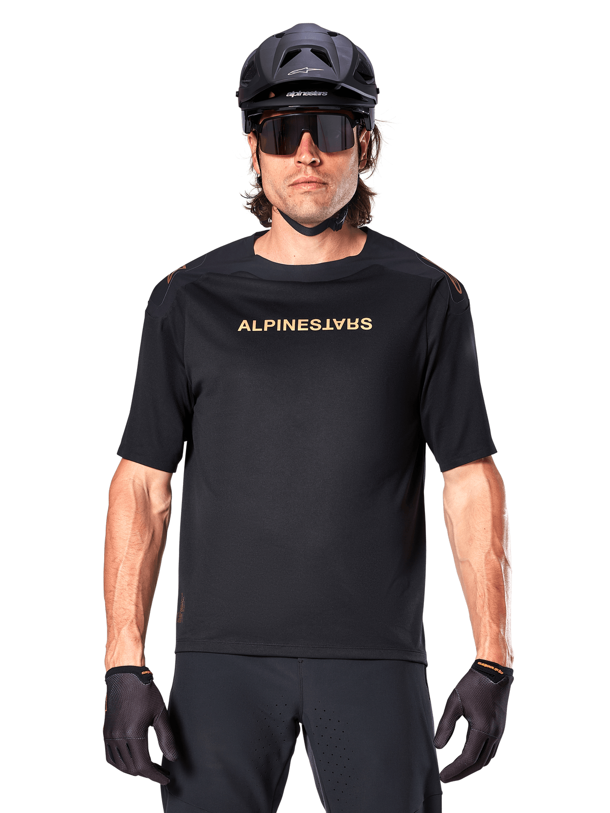Mountainbiker iført Alpinestars A-Aria Polartec Switch kortærmet trøje i sort med guldtonet brystlogo, sort MTB-hjelm, mørke performance-solbriller og matchende handsker, off-road cykeludstyr.