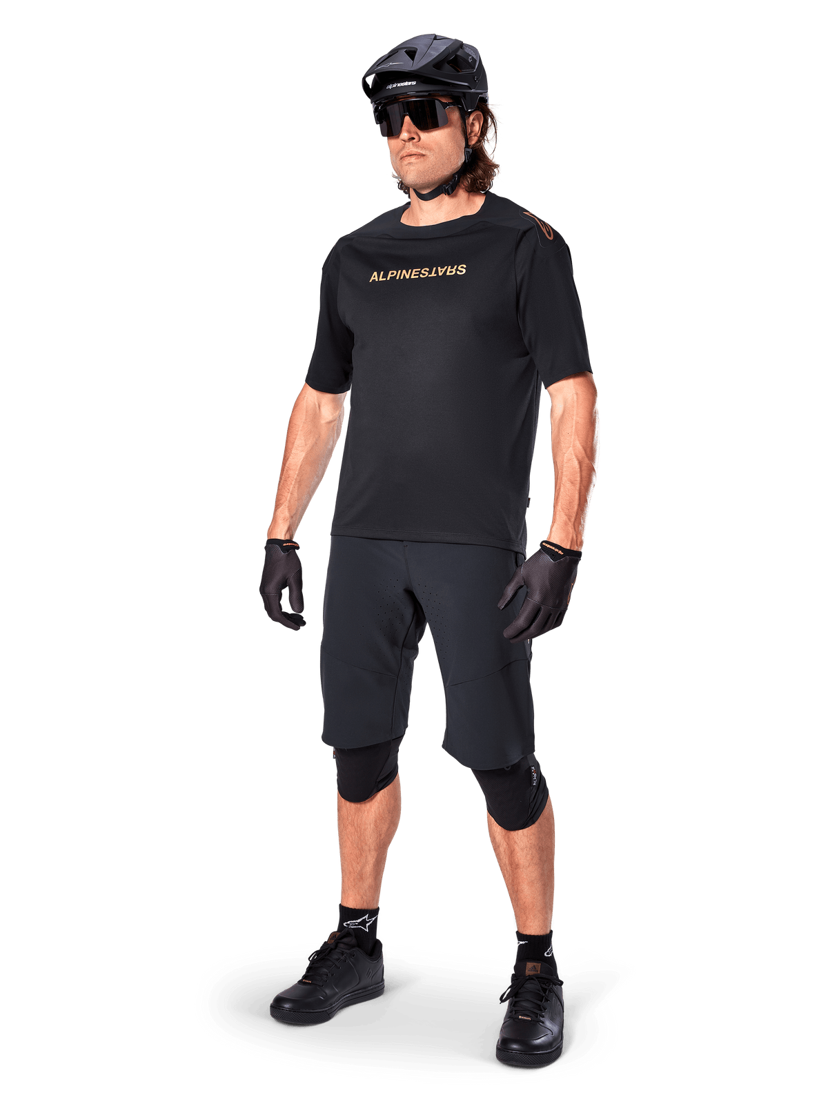 Alpinestars A-Aria Polartec Switch kortærmet trøje, sort med spejlvendt guld-branding på brystet, båret af en rytter med sorte cykelshorts, hjelm og knæbeskyttere, teknisk MTB-udstyr til terrænkørsel