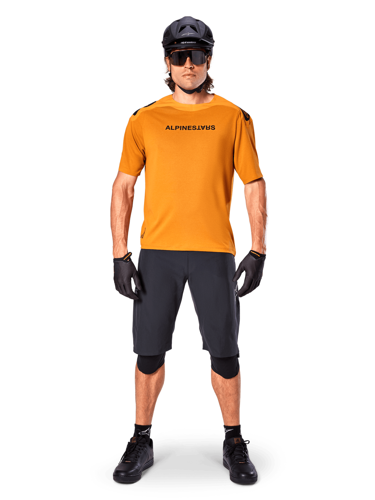 Male cyclist wearing the Alpinestars A-Aria Polartec Switch Short Sleeve Jersey in Dark Gold, paired with black MTB shorts, helmet, sunglasses, and gloves, professional mountain bike trail riding gear