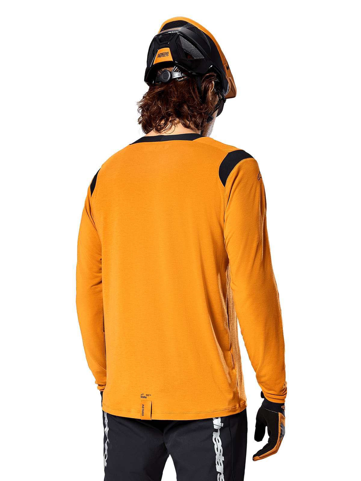 Alpinestars A-Dura Dri Wool langærmet jersey i Dark Gold, set bagfra af en rytter iført mountainbikehjelm og handsker, med sorte mesh-paneler på skuldrene og et længere rygstykke, teknisk cykeltøj til trailkørsel