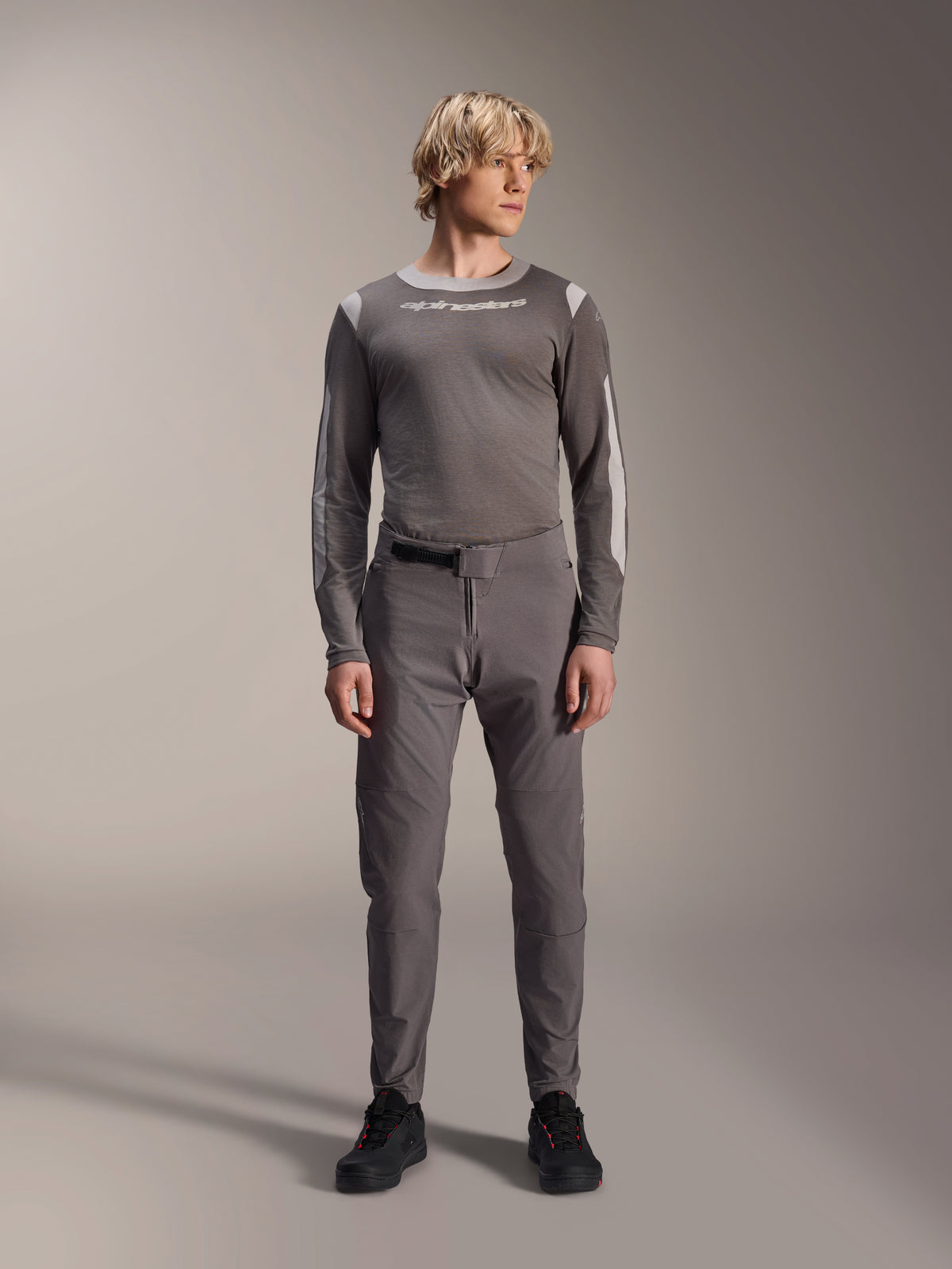 Alpinestars A-Dura Elite bukser, mørkegrå mountainbike-bukser, fuldkropsvisning, båret med en matchende grå langærmet performance-trøje med Alpinestars-logo, sorte sko med røde detaljer, atletisk cykeloutfit