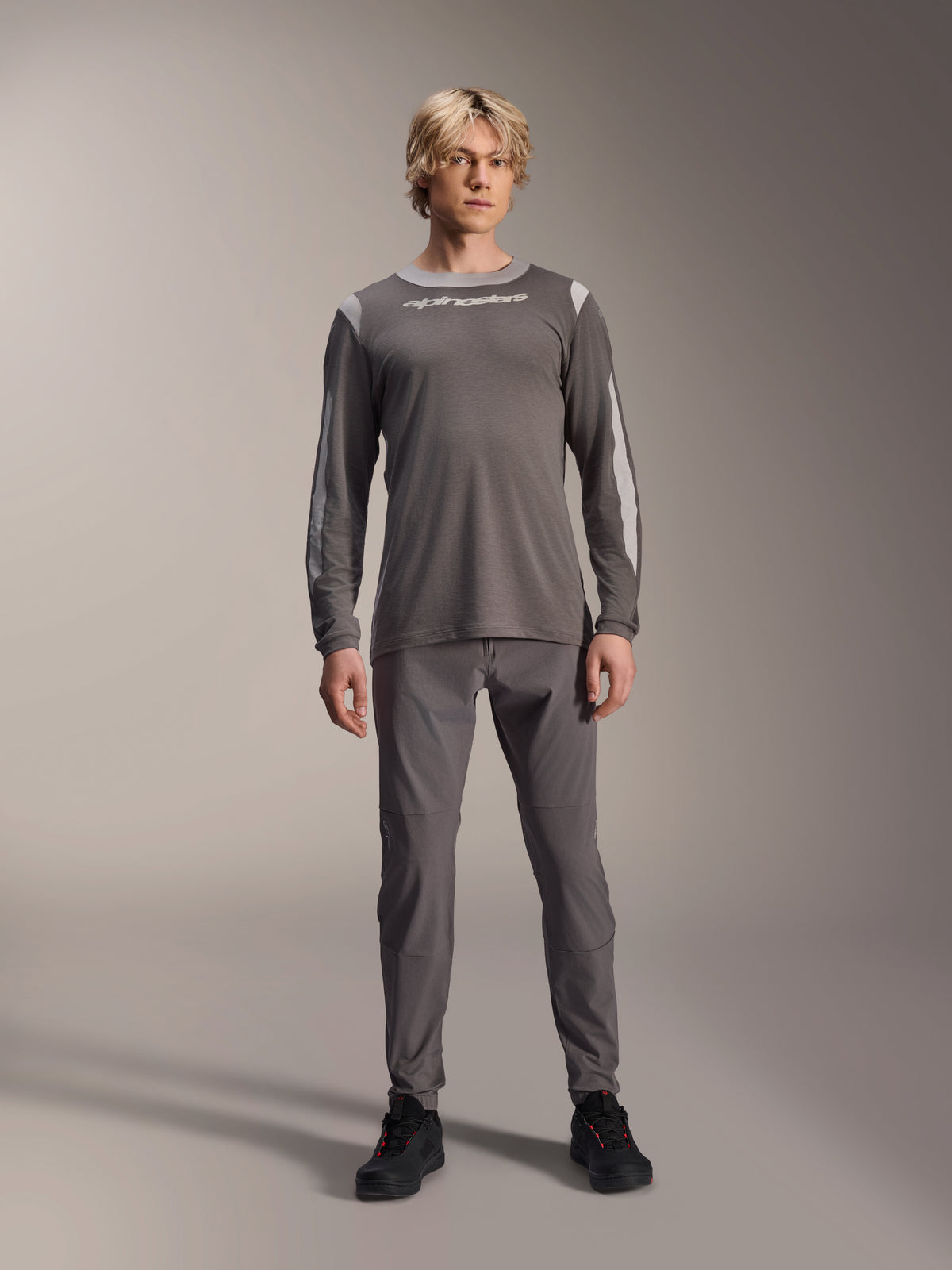 Alpinestars A-Dura Dri Wool Long Sleeve Jersey, Dark Gray, worn by model with matching gray pants and black shoes, white Alpinestars branding on chest, light gray mesh panels on shoulders and sleeves, technical mountain bike gear