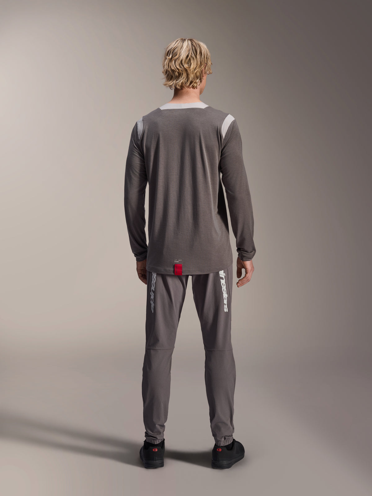 Alpinestars A-Dura Dri Wool Jersey - Long Sleeve, Dark Gray, rear view on model, featuring light gray mesh panels on shoulders and collar, dropped tail hem with a small red brand tag, worn with matching gray cycling pants.