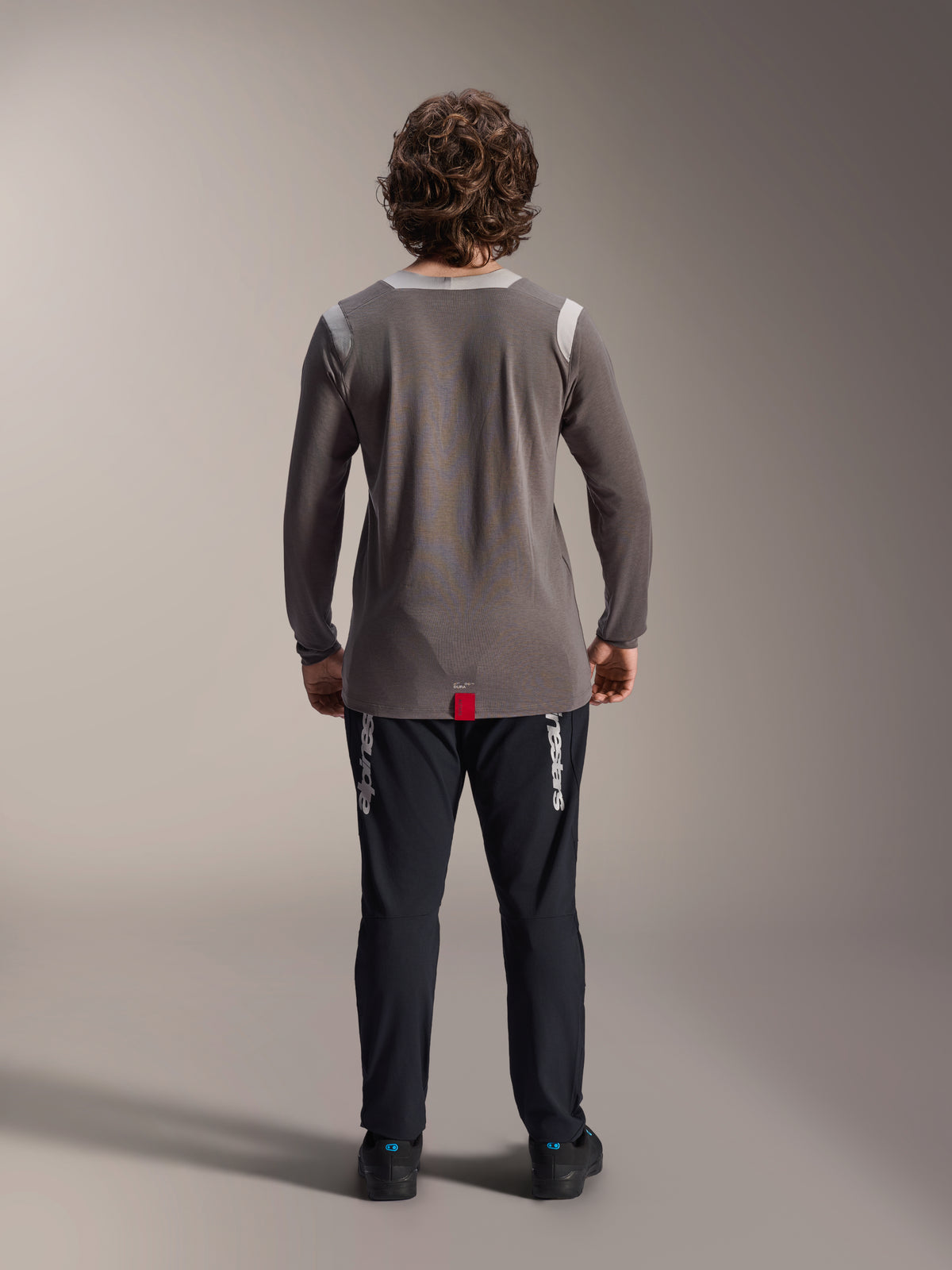 Alpinestars A-Dura Elite Pants and A-Dura Dri Wool Long Sleeve Jersey, Black pants with white branding, Grey technical jersey, rear view of mountain bike outfit, durable off-road cycling apparel