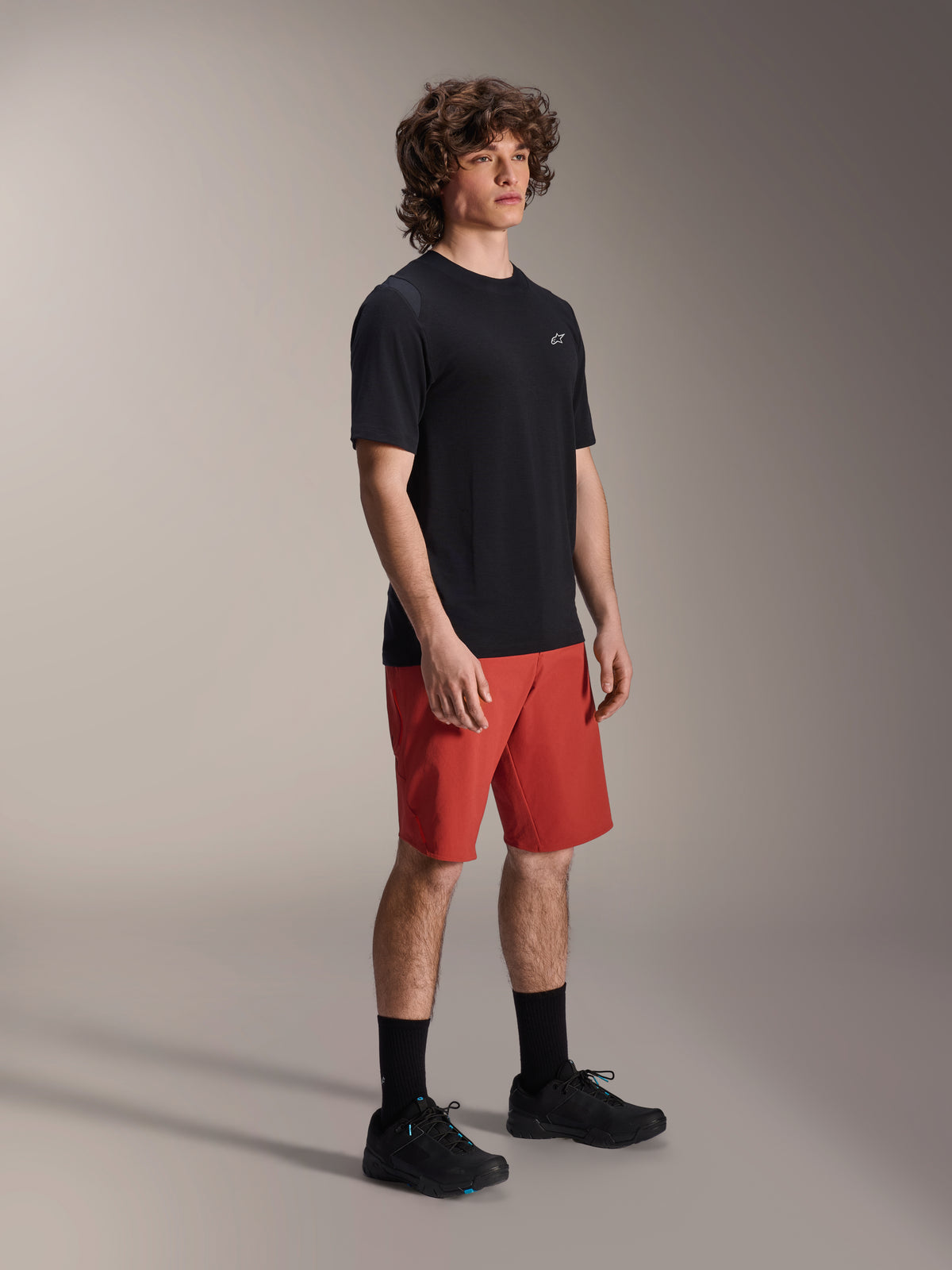 Male model wearing Alpinestars A-Dura Elite Shorts in Dark Orange and A-Dura Dri Wool Short Sleeve Jersey in Black, mountain bike performance gear, paired with black socks and shoes, athletic design for off-road cycling.