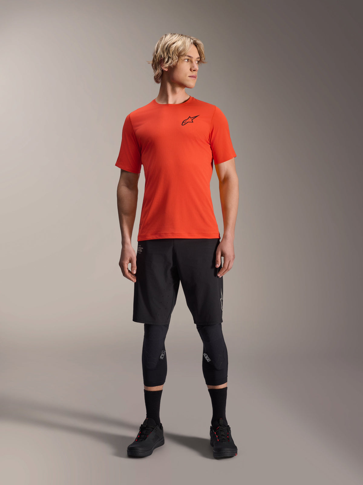 Alpinestars A-Aria Astar kortærmet trøje, Spicy Orange, båret af model med sorte mountainbike-shorts og knæbeskyttere, letvægts og åndbart performance-cykeltøj til MTB