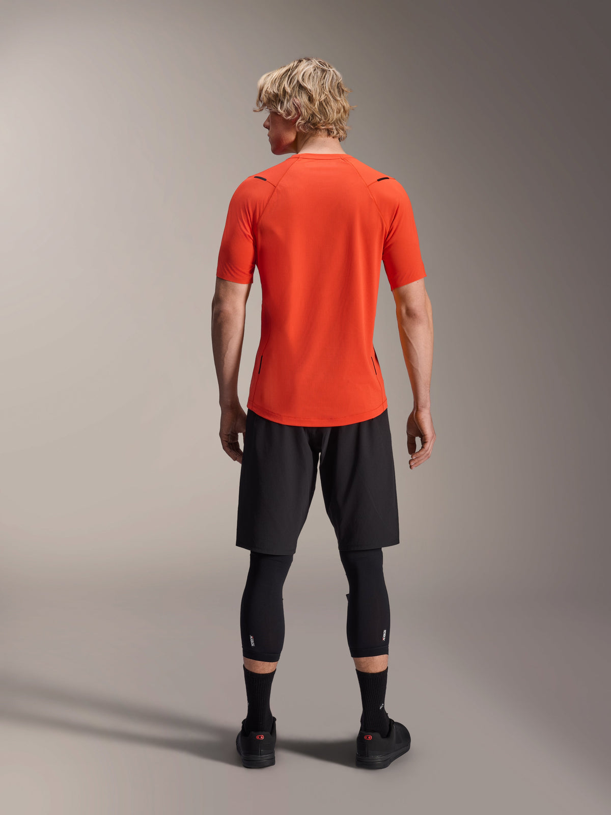 Alpinestars A-Aria Astar jersey, kortærmet MTB-trøje, Spicy Orange, set bagfra, viser performance fit og længere fald bagpå, kombineret med sorte cykelshorts og leggings