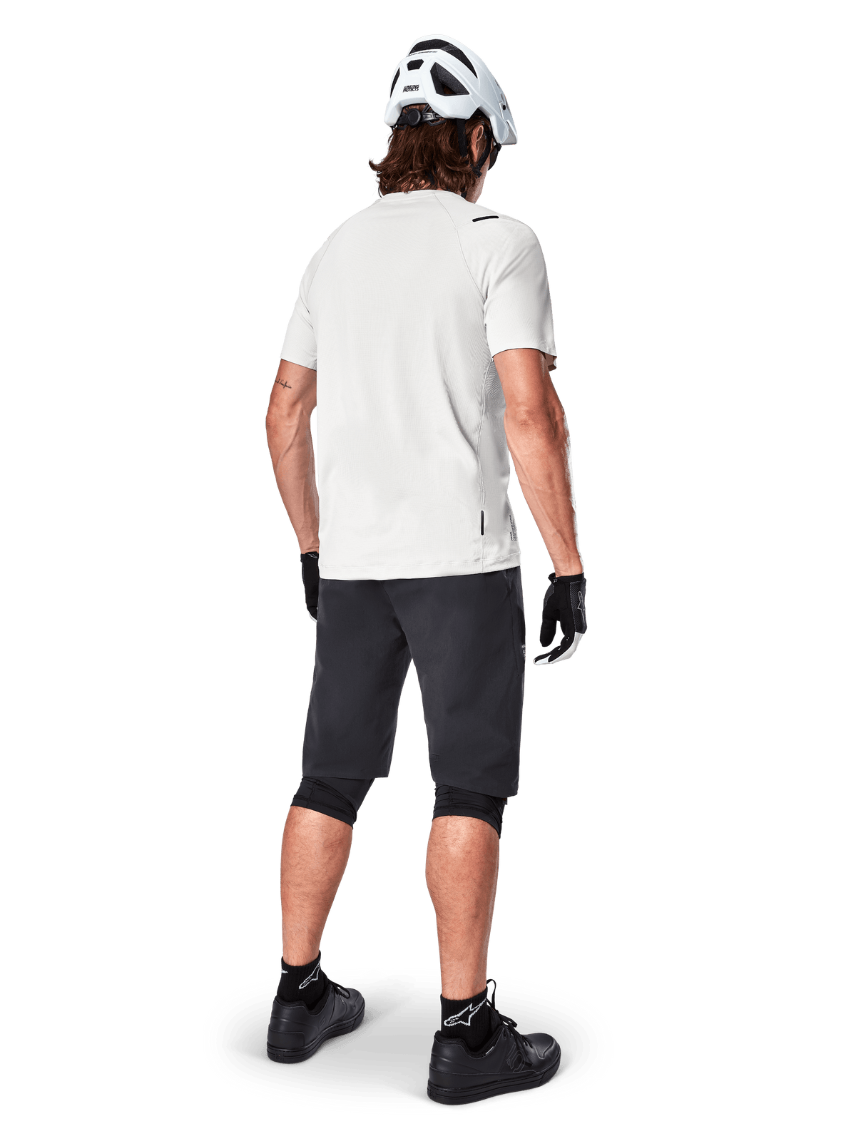 Cyclist wearing the Alpinestars A-Aria Astar Short Sleeve Jersey in White Dove, rear view, paired with black MTB shorts, knee guards, and a white helmet, lightweight and breathable gear for off-road mountain biking