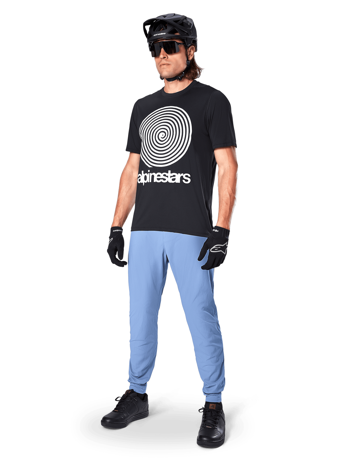 Alpinestars A-Dura Oscar kortærmet jersey, sort MTB-jersey med stor hvid vintage spiralgrafik, båret af en rytter med sort hjelm, solbriller, sorte handsker og lyseblå bukser, mountainbike-udstyr