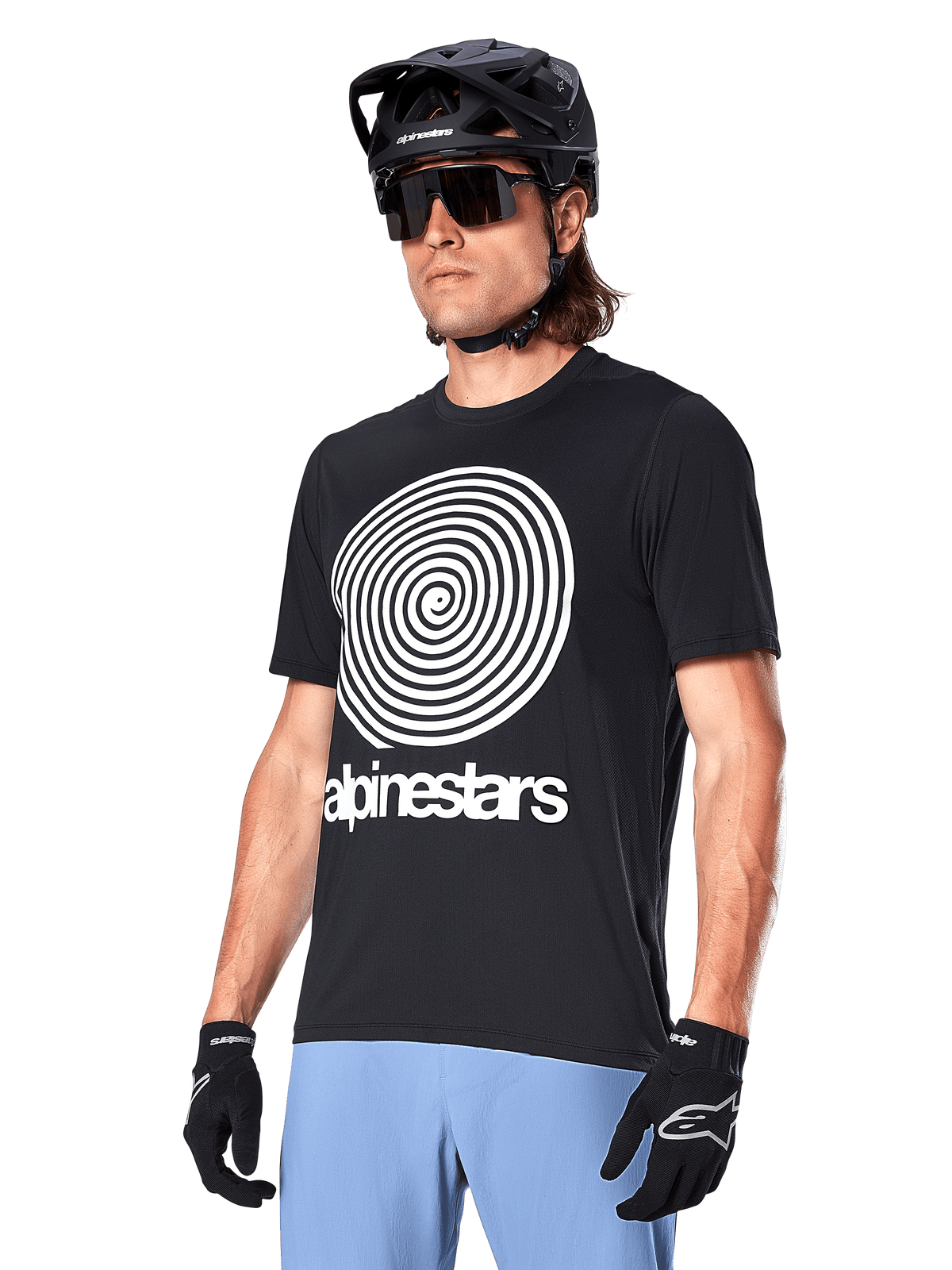Alpinestars A-Dura Oscar kortærmet jersey, sort, med stor hvid spiralgrafik og Alpinestars-branding på brystet, båret af en rytter med sort MTB-hjelm, solbriller og lyseblå bukser