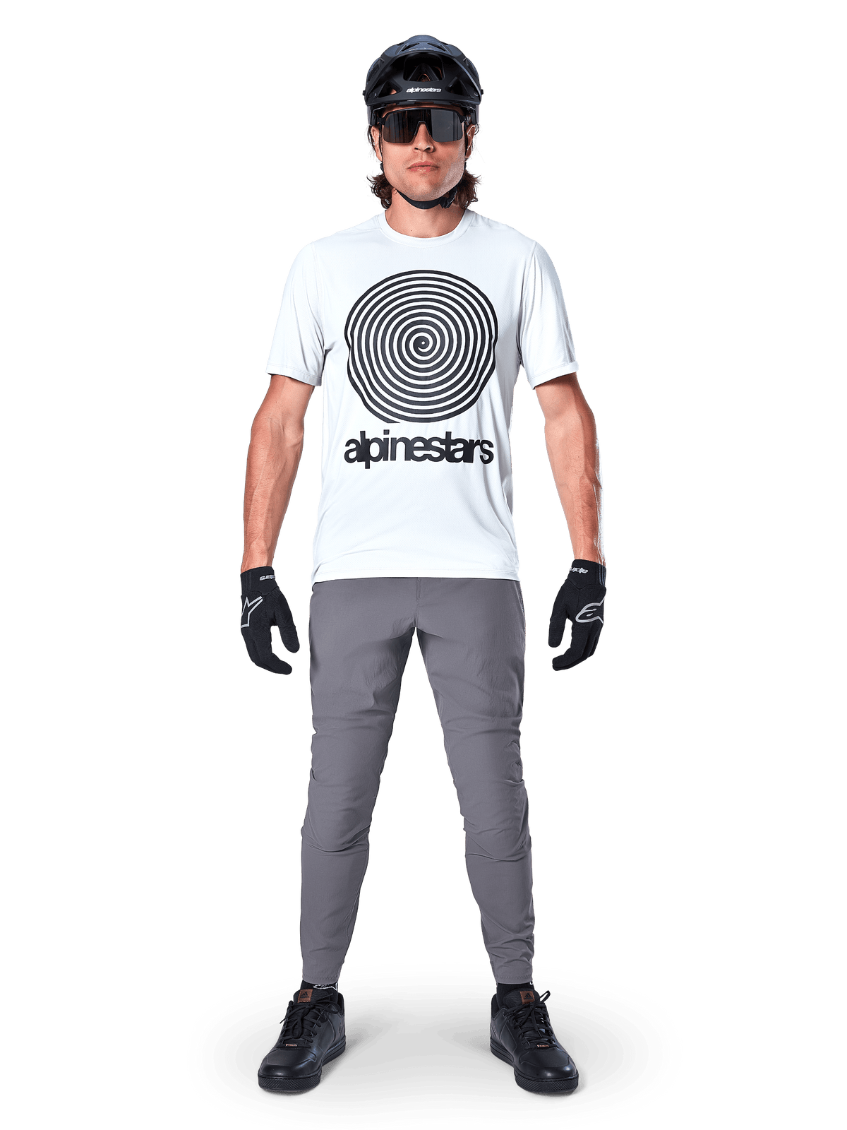 Mountainbiker iført Alpinestars A-Dura Oscar jersey, kortærmet, White Dove med stort sort spirallogo, kombineret med grå bukser, sort hjelm, solbriller og sorte handsker, performance MTB trail-udstyr