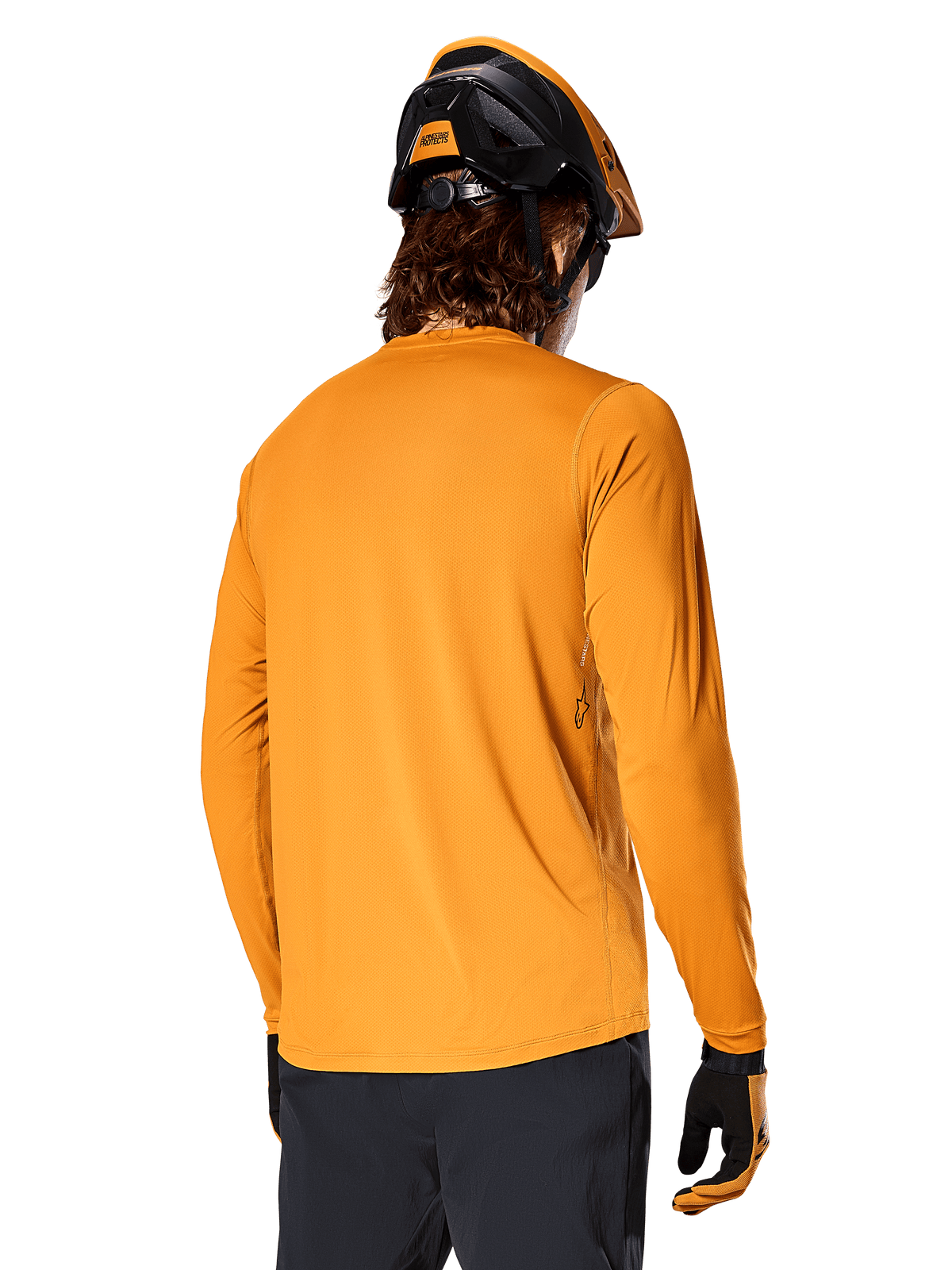 Alpinestars A-Dura Rocker langærmet trøje, Dark Gold, rytter set bagfra iført sort og orange MTB-hjelm, mørke bukser og matchende handsker, afslappet mountainbike-performance-beklædning