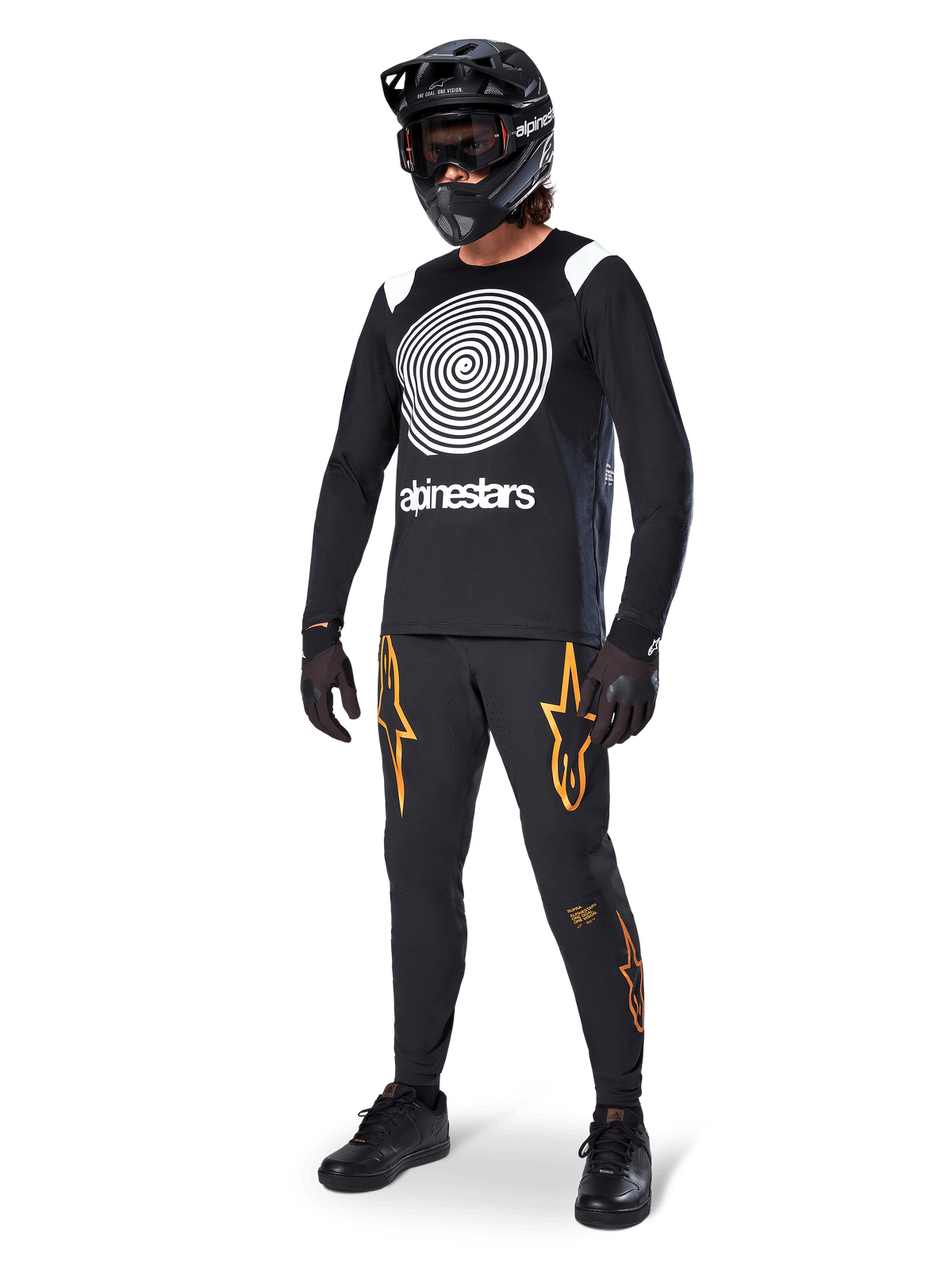 MTB rider wearing Alpinestars A-Supra Oscar Long Sleeve Jersey in Black, featuring the white vintage Oscar spiral graphic, black pants with orange star logos, black full-face helmet with goggles, and black gloves, professional mountain biking gear