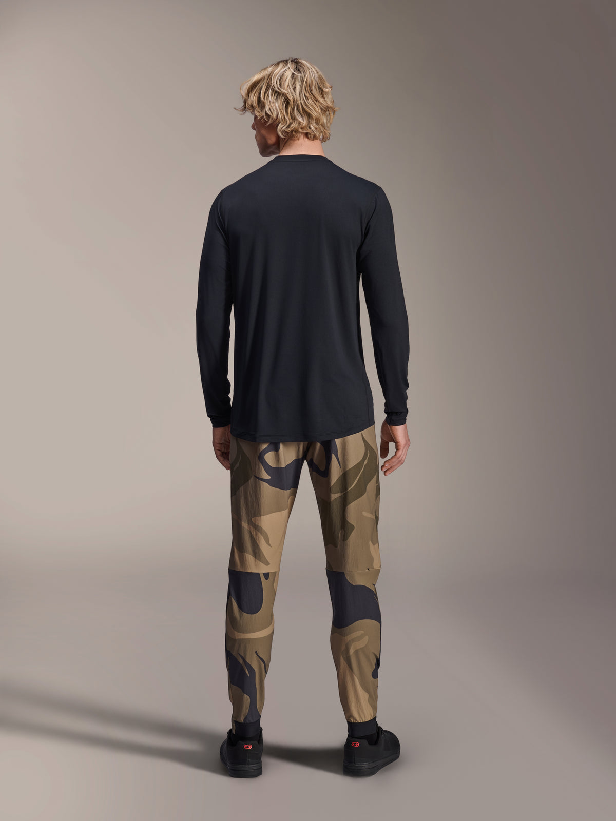 Alpinestars A-Dura Astar Jersey, langærmet trøje, sort, set bagfra af model iført camouflagebukser, med et længere rygstykke og almindelig pasform til mountainbike